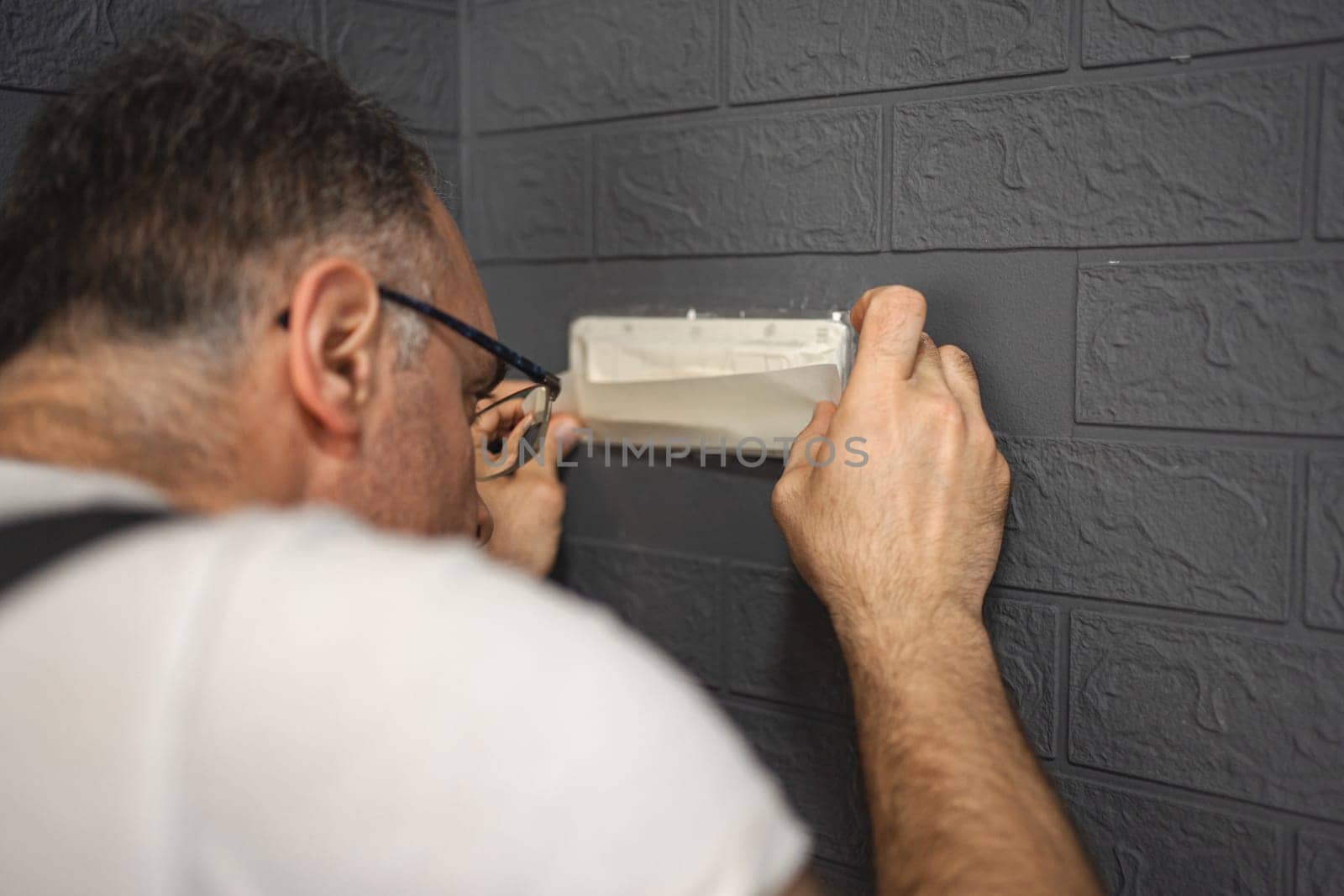 Man carefully tapes a piece of masking tape to switches before he starts painting the walls