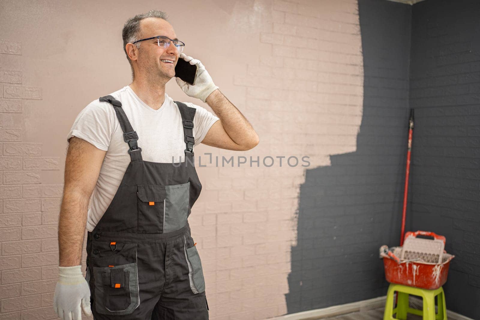 A man wearing overalls is engaged in a phone conversation on his cell phone. He appears focused as he communicates, standing in an outdoor setting.