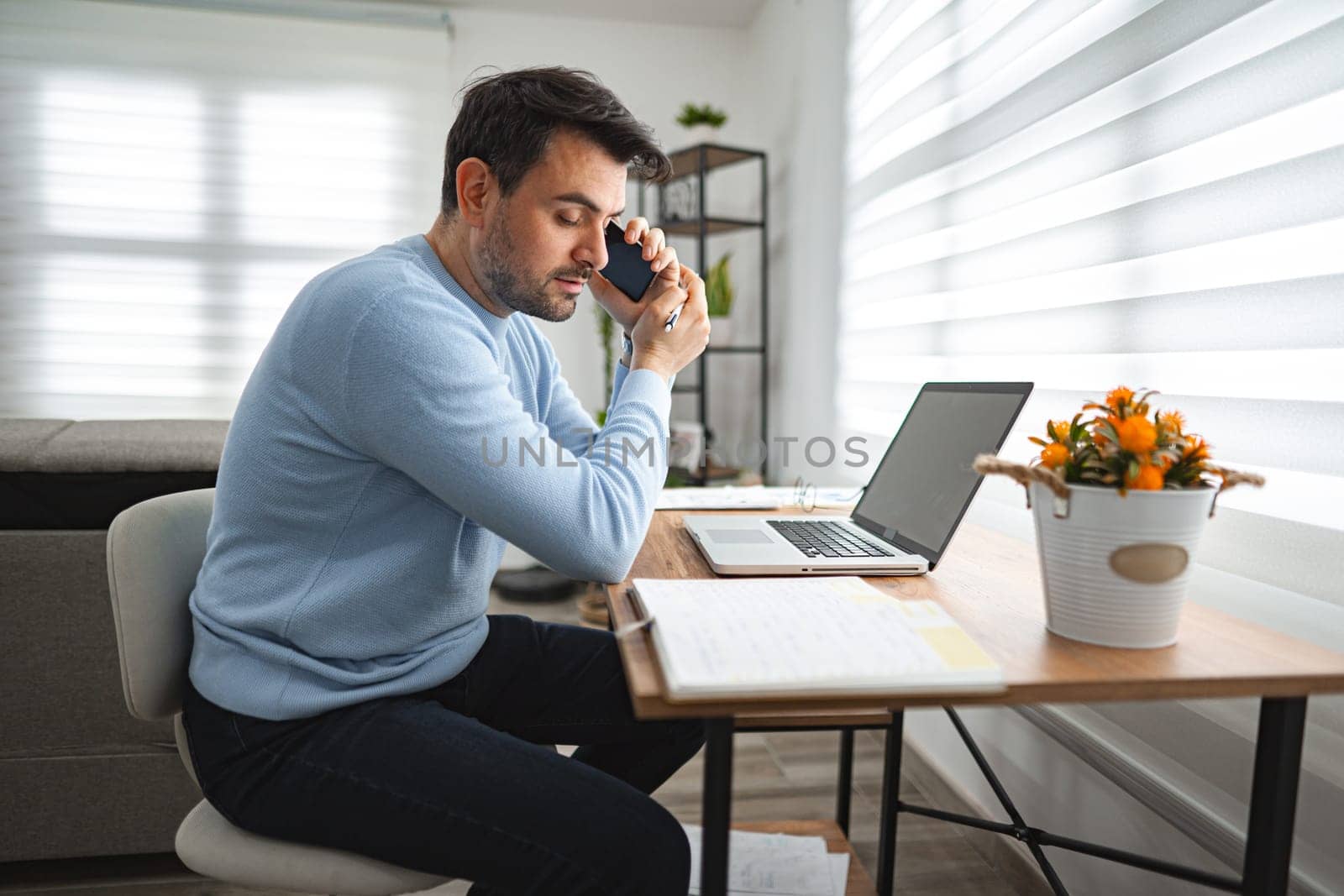 A man is seated at a desk, engaged in a conversation on his cell phone. He appears focused and attentive as he communicates with the person on the other end of the call.