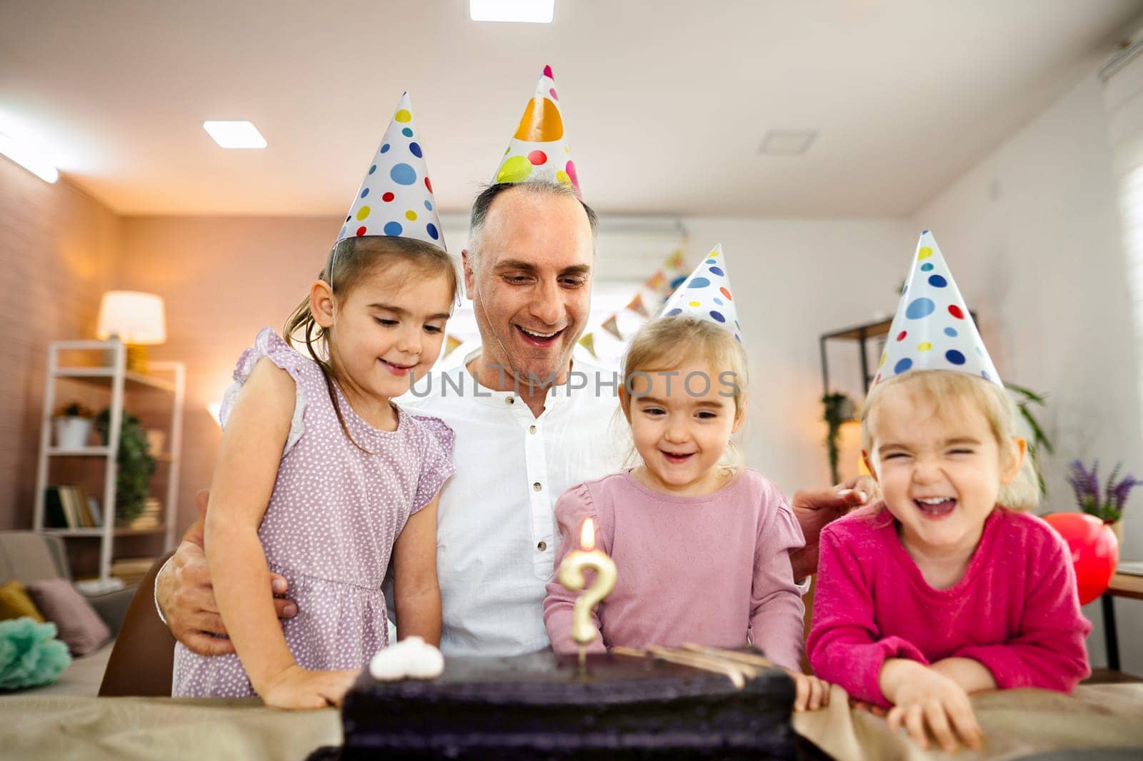 A cheerful gathering of three young girls around a cake with candles.