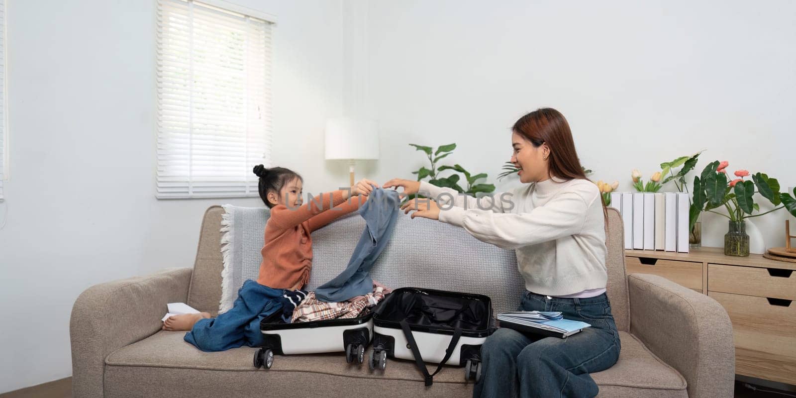 A nurturing scene where a mother helps her daughter with organizing clothes in the suitcase, highlighting teamwork in travel planning.