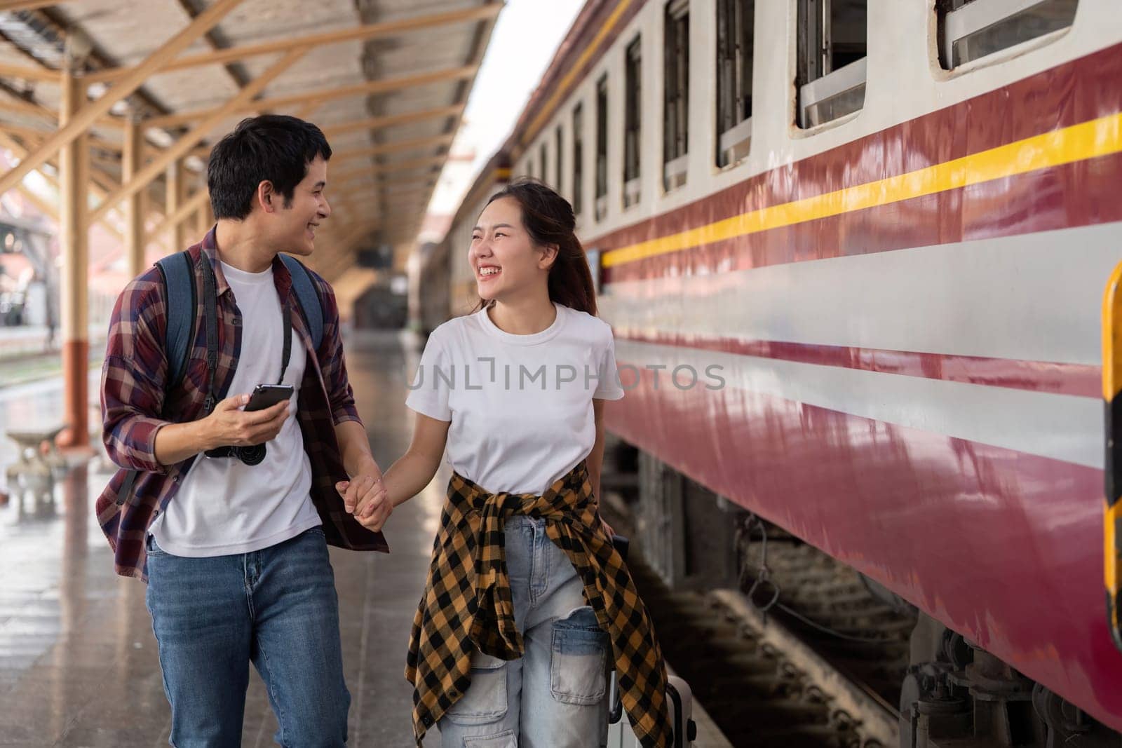 As they stroll through the train station hand in hand, a couple shares laughter, embodying love and excitement for their upcoming journey.