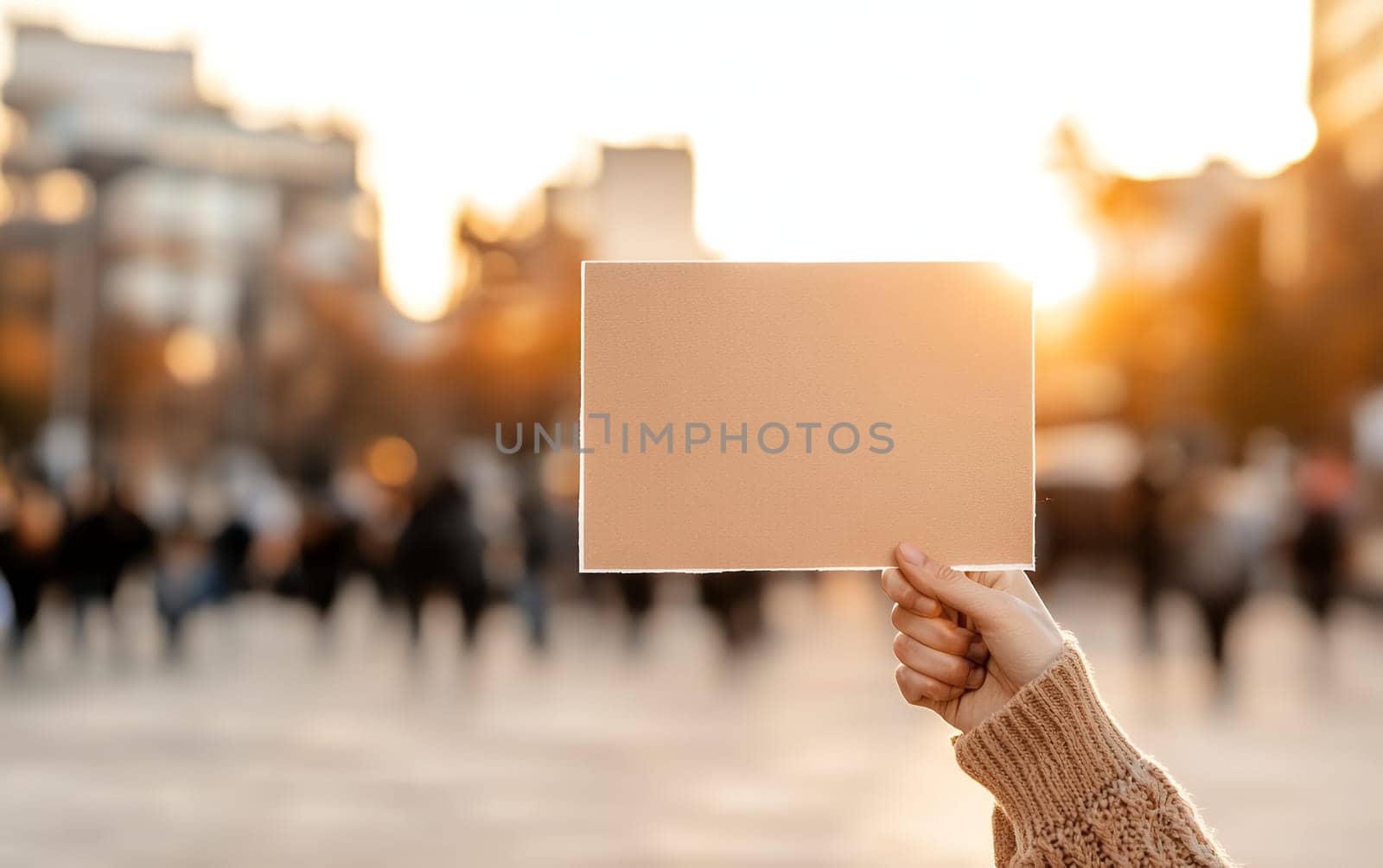 Hand holding blank sign card against blurred city sunset background.
