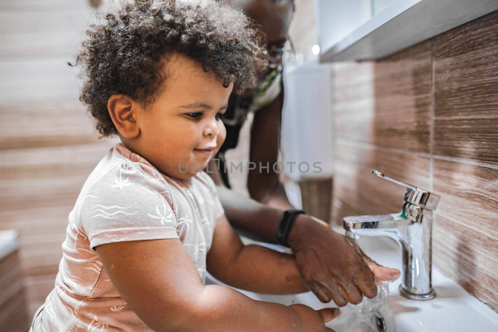 A toddler engages in handwashing with guidance from an adult.