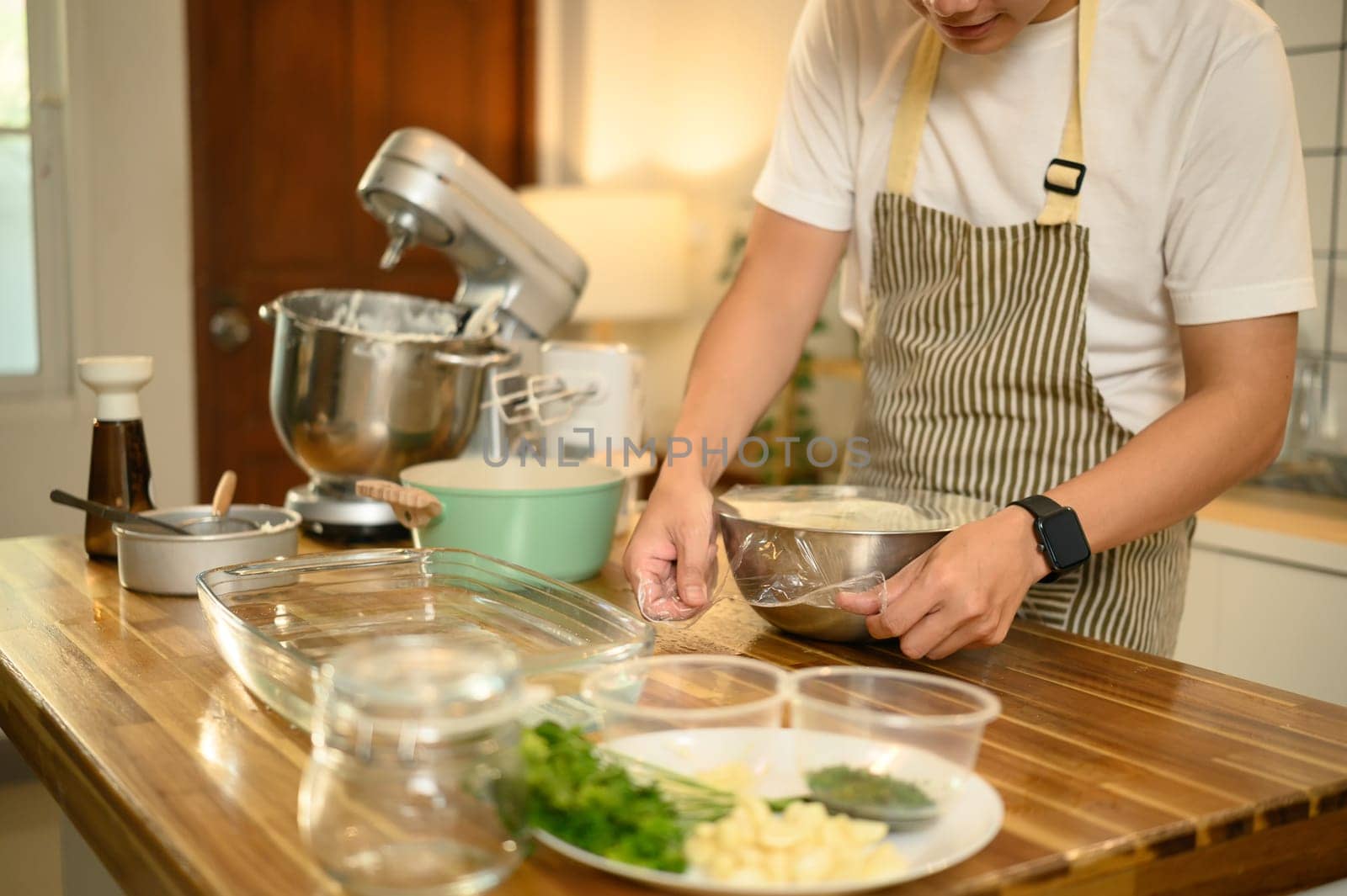 Man covering a mixing bowl of whipped cream with plastic wrap, ready for refrigeration.