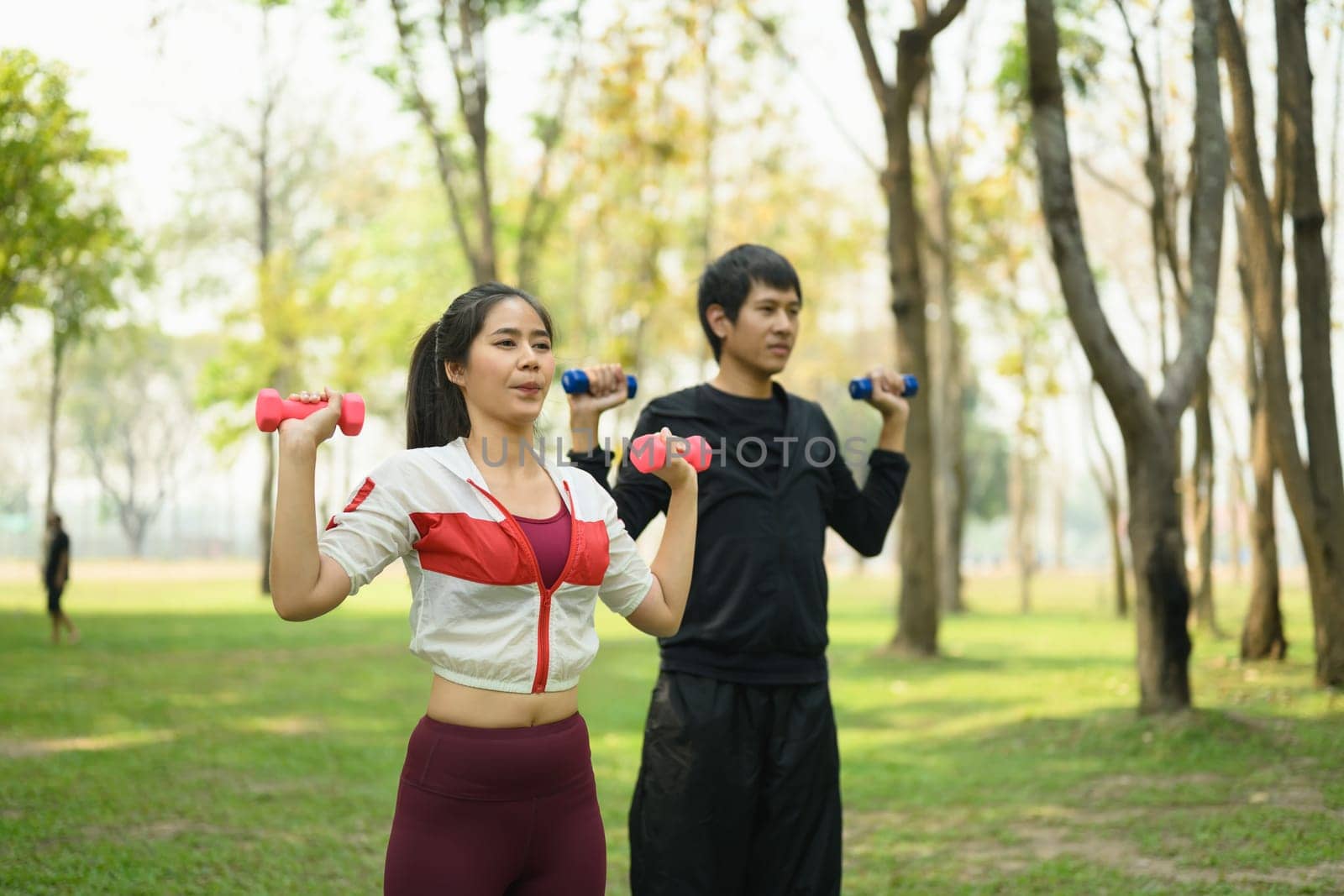 Man and woman exercising with dumbbells in a park. Healthy living and fitness concept.