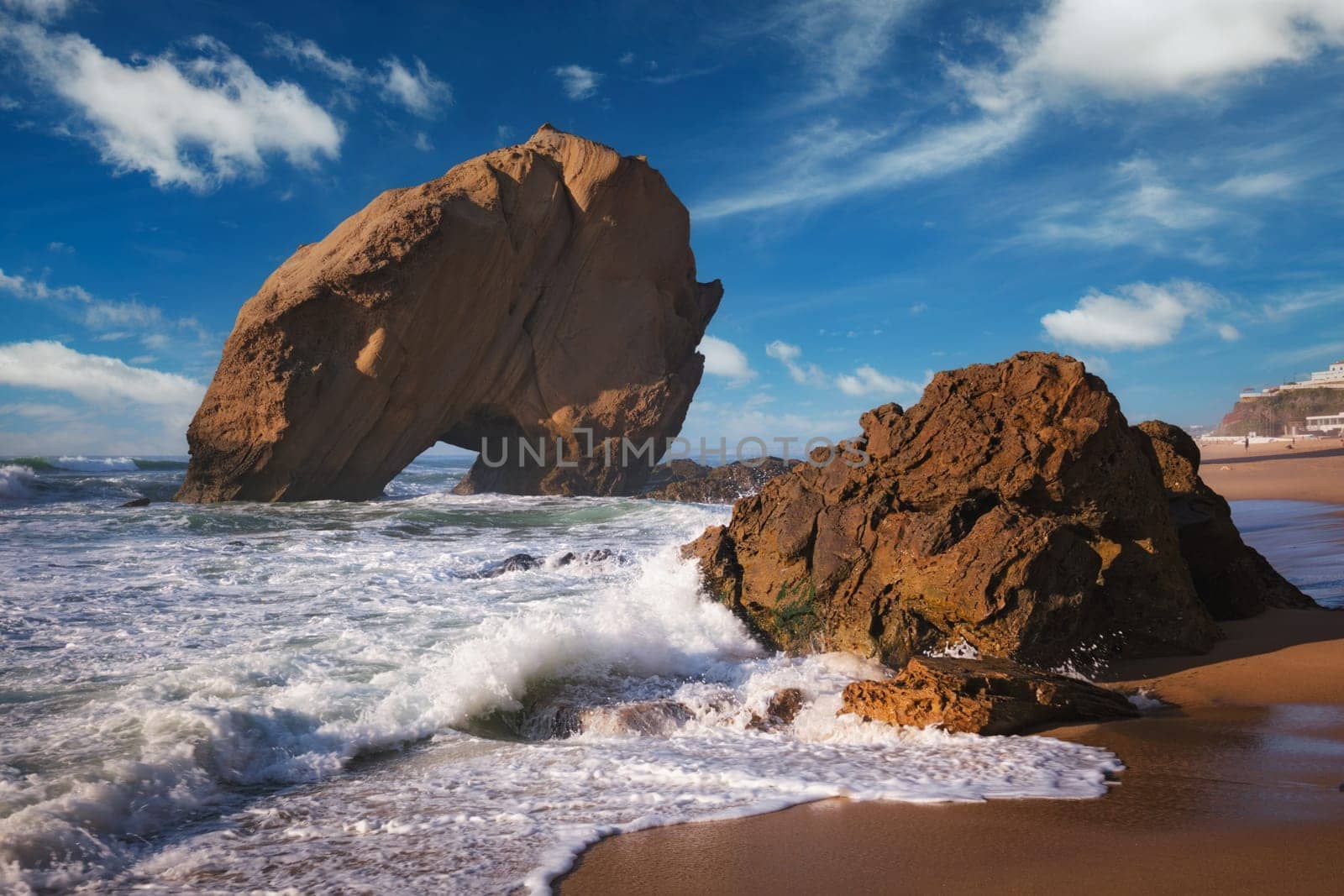 Penedo do Guincho, a large boulder rock arch at Praia da Santa Cruz, Portugal, with ocean waves and sandy beach