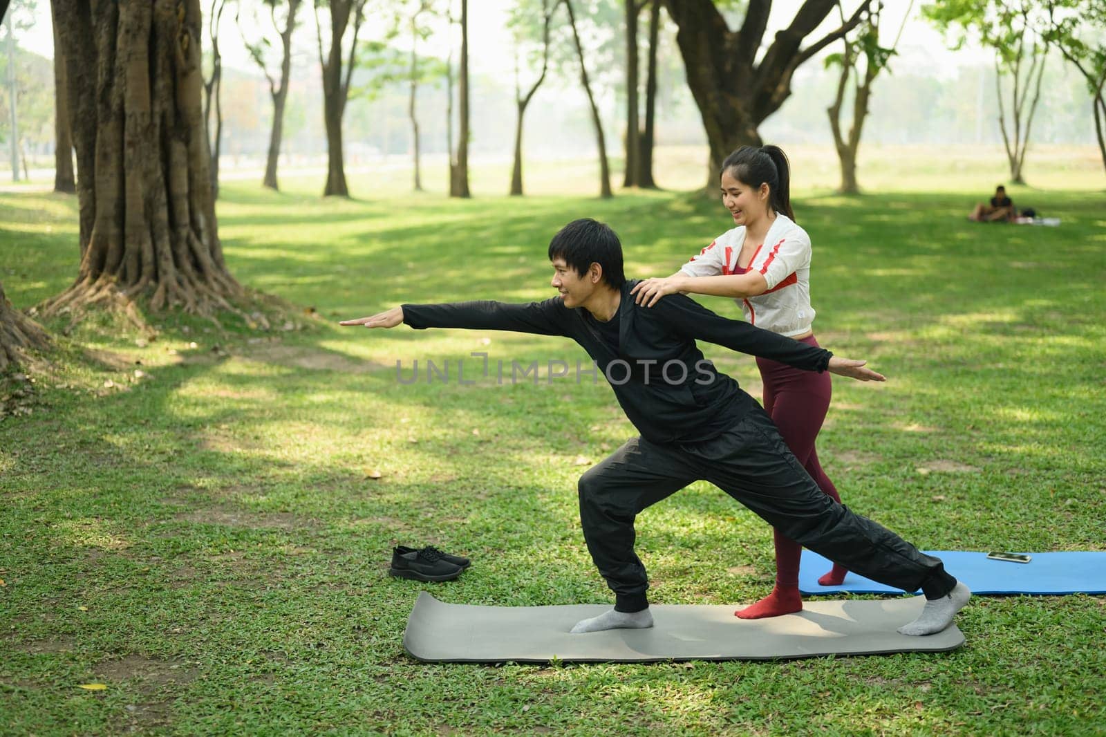 Happy young couple practicing yoga together in the park. Healthy living and mindfulness concept.