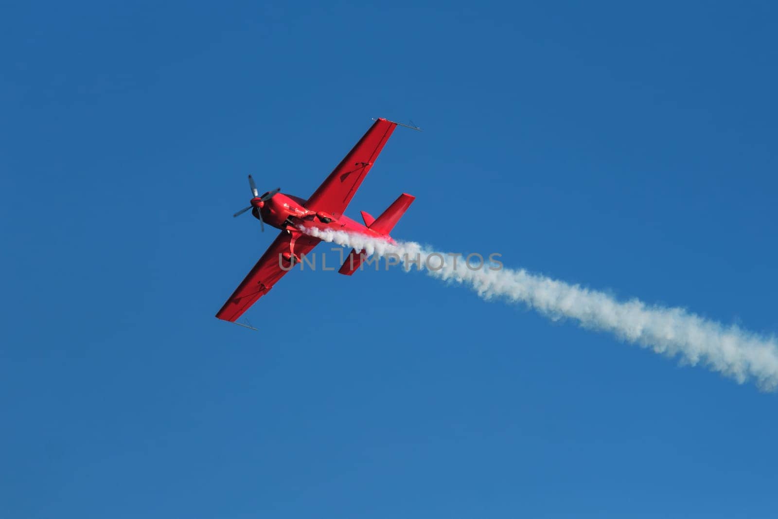 Red stunt aerobatic plane performing stunts in blue sky. Concept of speed, difficulty, precision, risk
