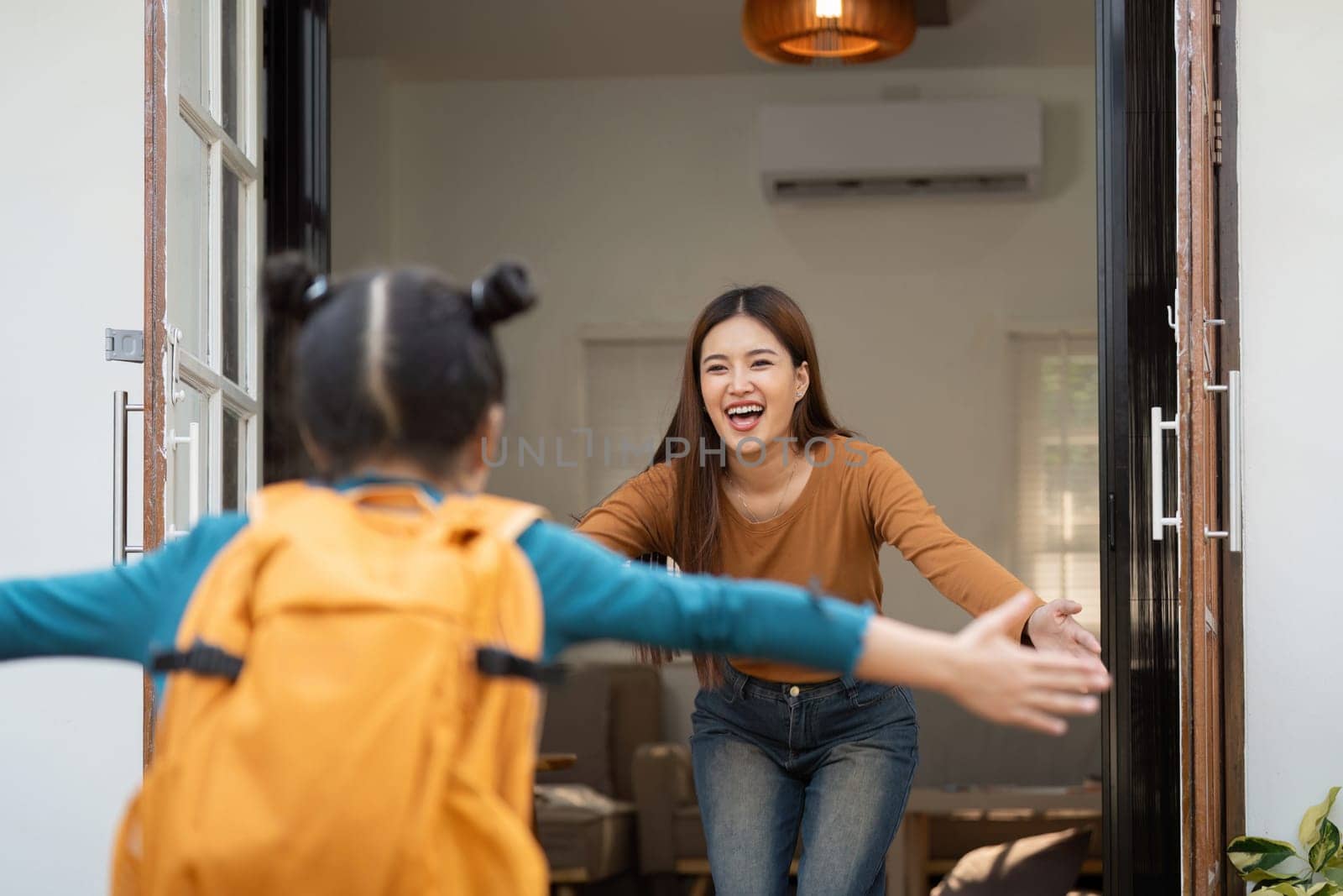 The girl runs happily towards her mother, arms wide open, capturing a joyful moment before an exciting day at school.