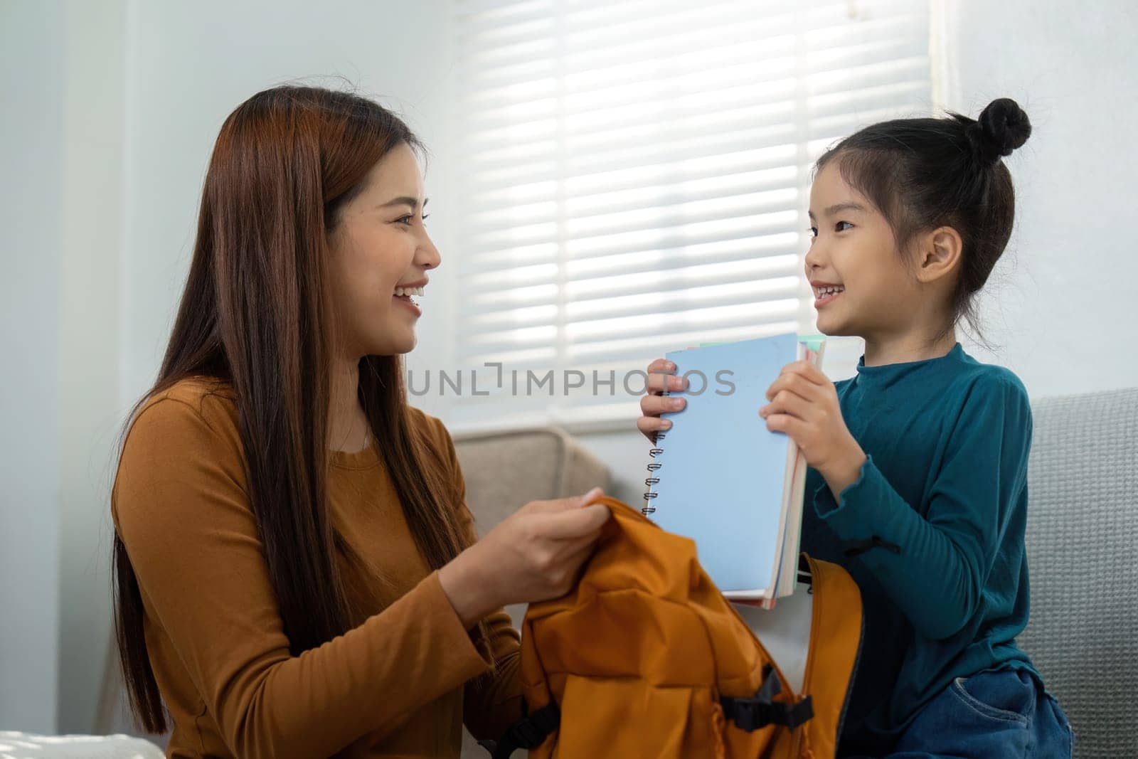 A young girl excitedly shows her notebook to a smiling woman, embodying the joy of learning and the vital role of parental support during school preparations.