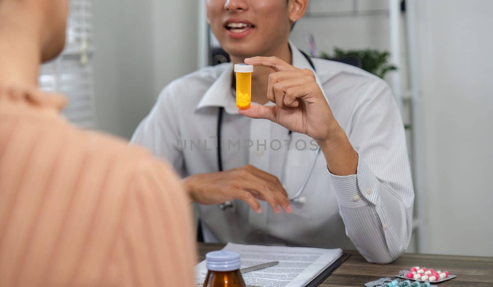 A healthcare professional discusses medication, holding a prescription bottle during a consultation with a patient.