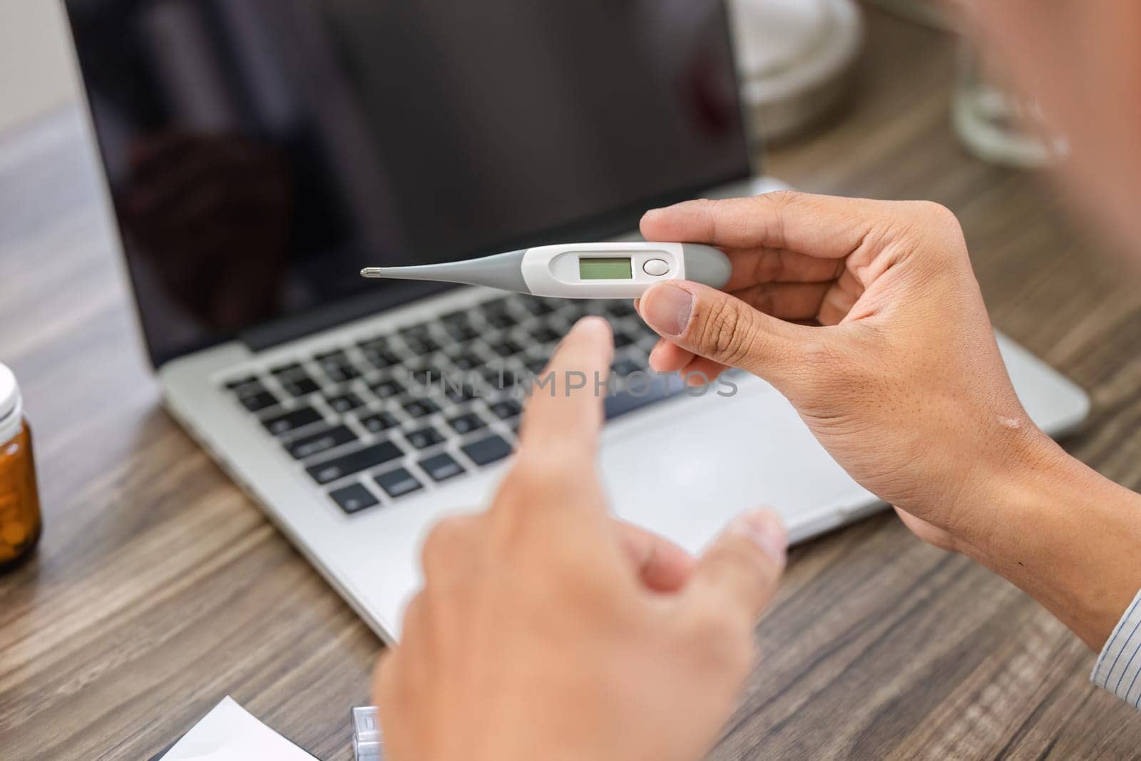 An individual checks their temperature with a digital thermometer while discussing their health with a healthcare provider, focusing on accurate diagnosis.