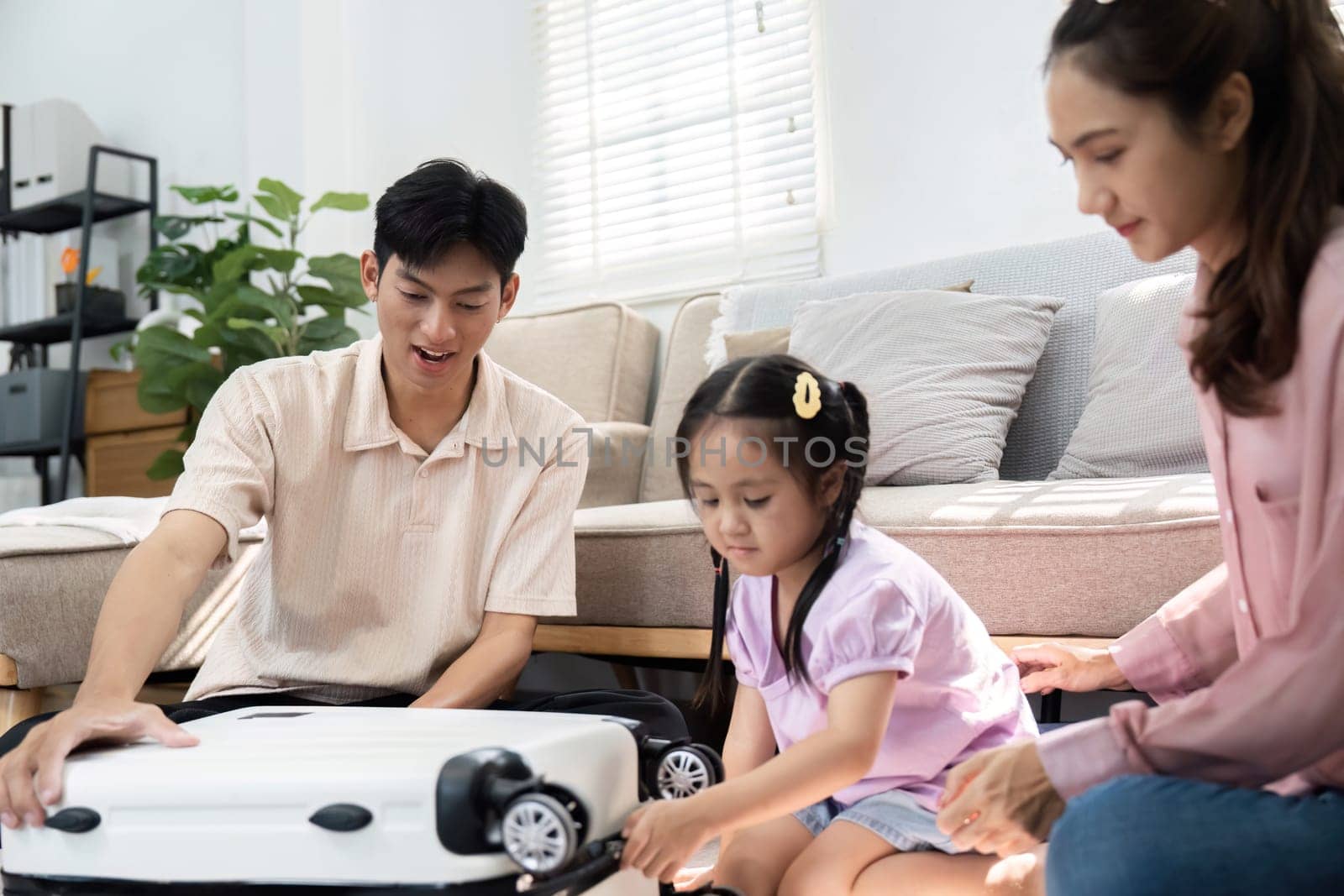 The family shares a light-hearted moment as their daughter plays with a toy suitcase, symbolizing the excitement and anticipation of their travels together.