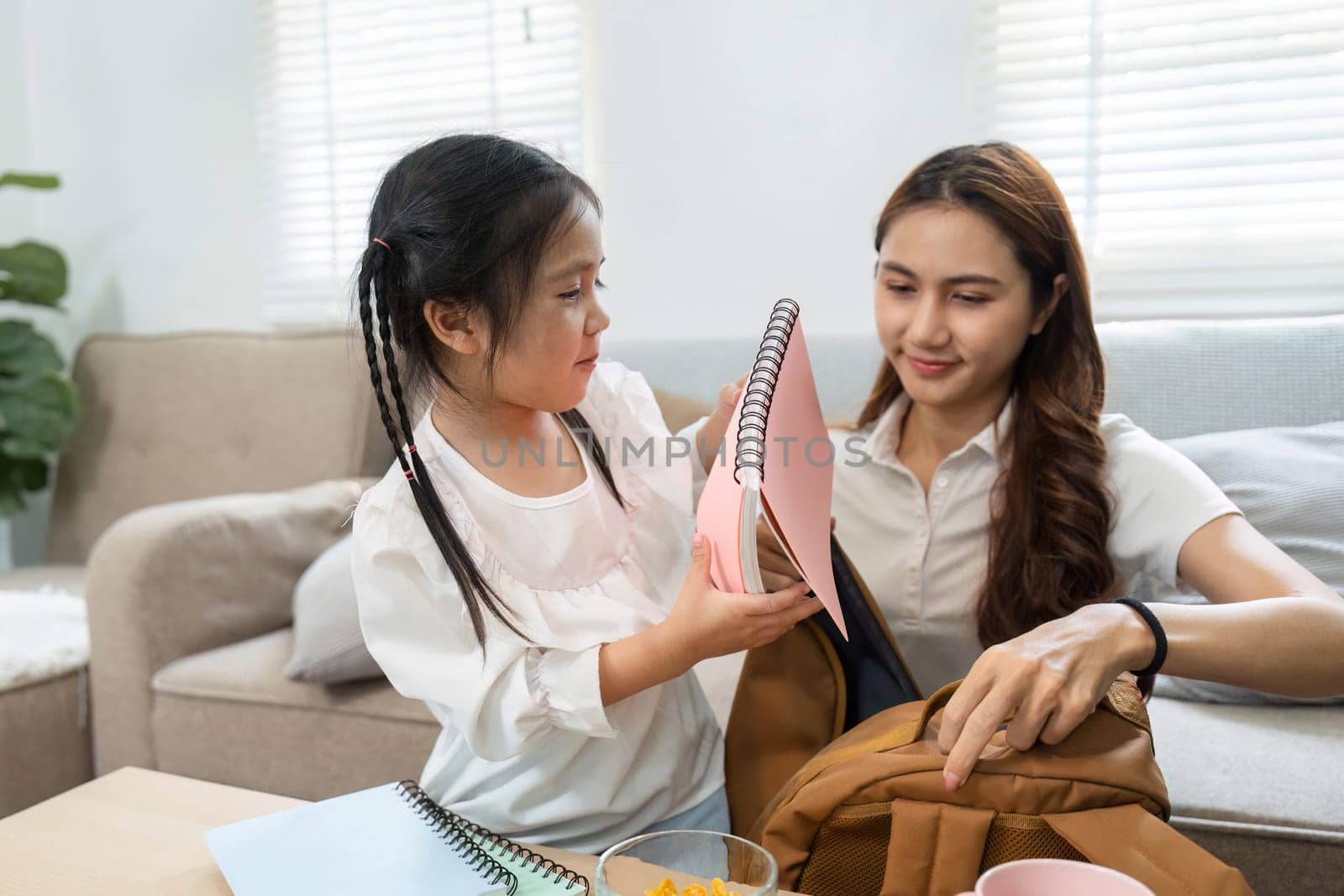 The girl shows excitement as she shares her colorful notebooks with her mother, displaying her enthusiasm for school and learning.