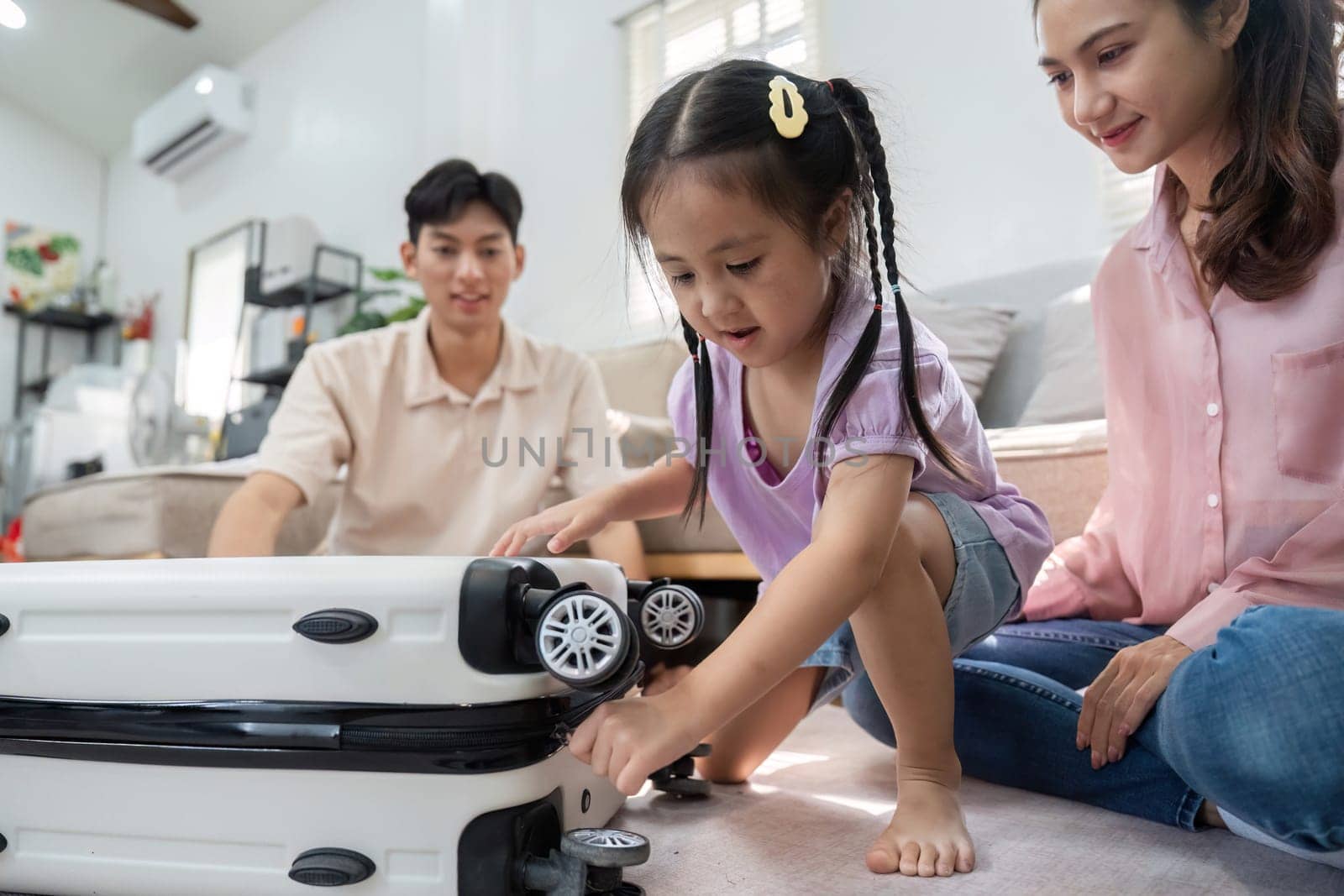 In a cozy living room, a girl joyfully explores a suitcase while her parents support her curiosity and playfulness, representing family love.