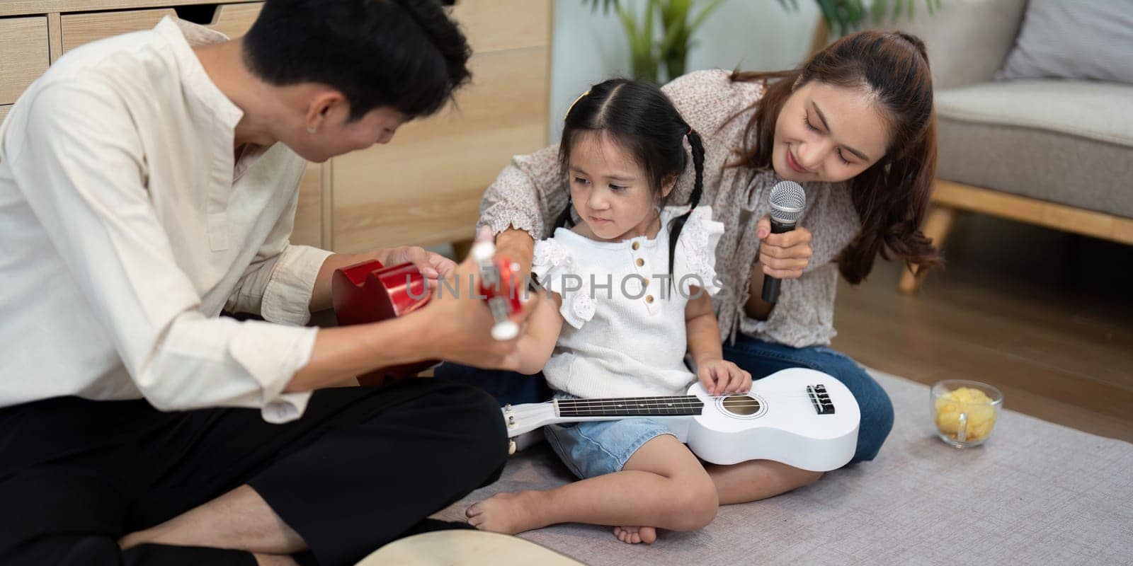An energized atmosphere as a father plays the guitar, while both his wife and daughter join in, showcasing their familial love through playful music.