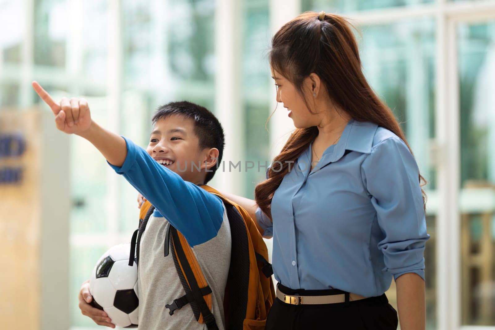 The mother guides her son as they walk together towards school, celebrating his passion for soccer with smiles and laughter.