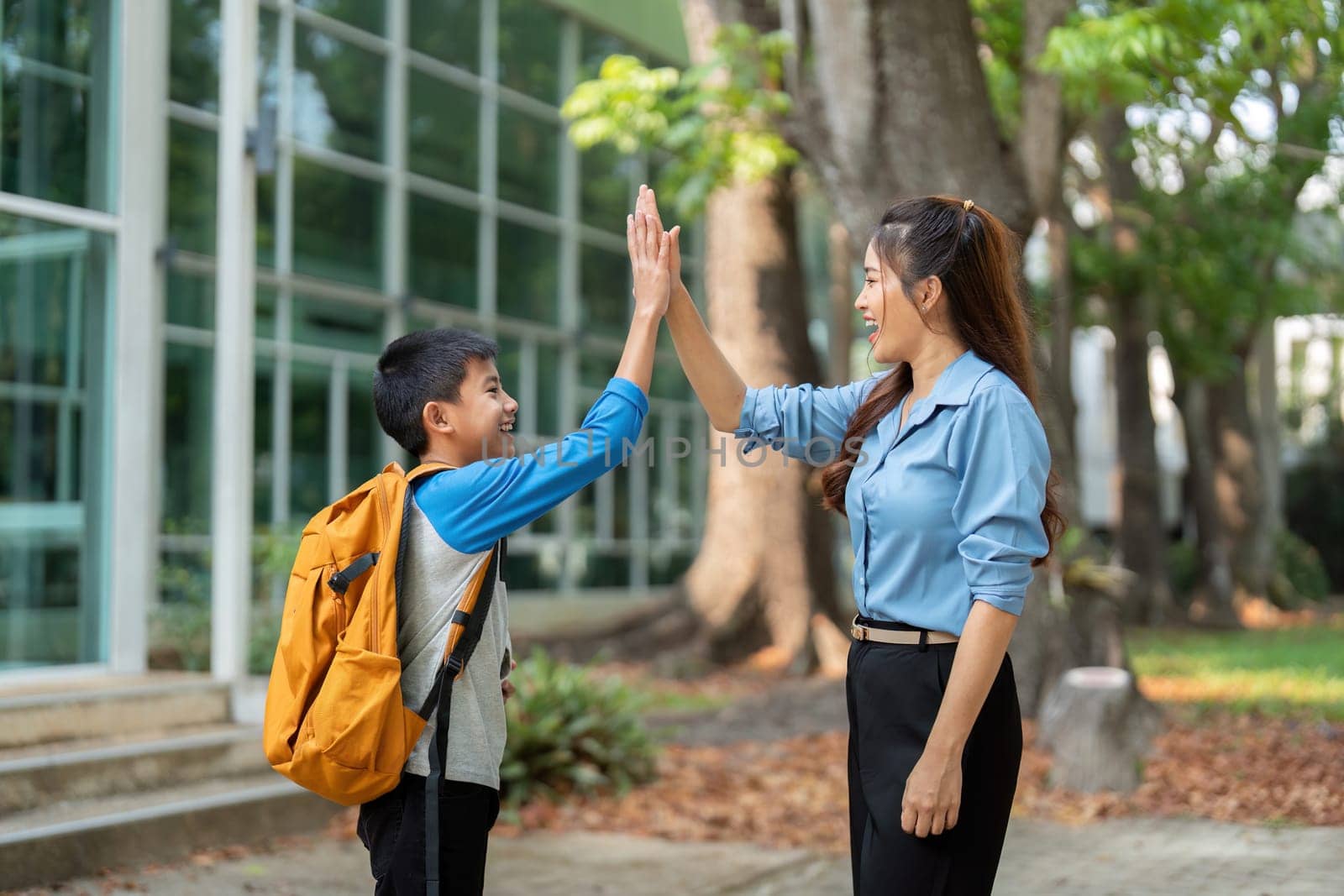 A mother and her son exchange high fives, celebrating the start of another school day together. This image represents joy, encouragement, and the importance of family support in education.