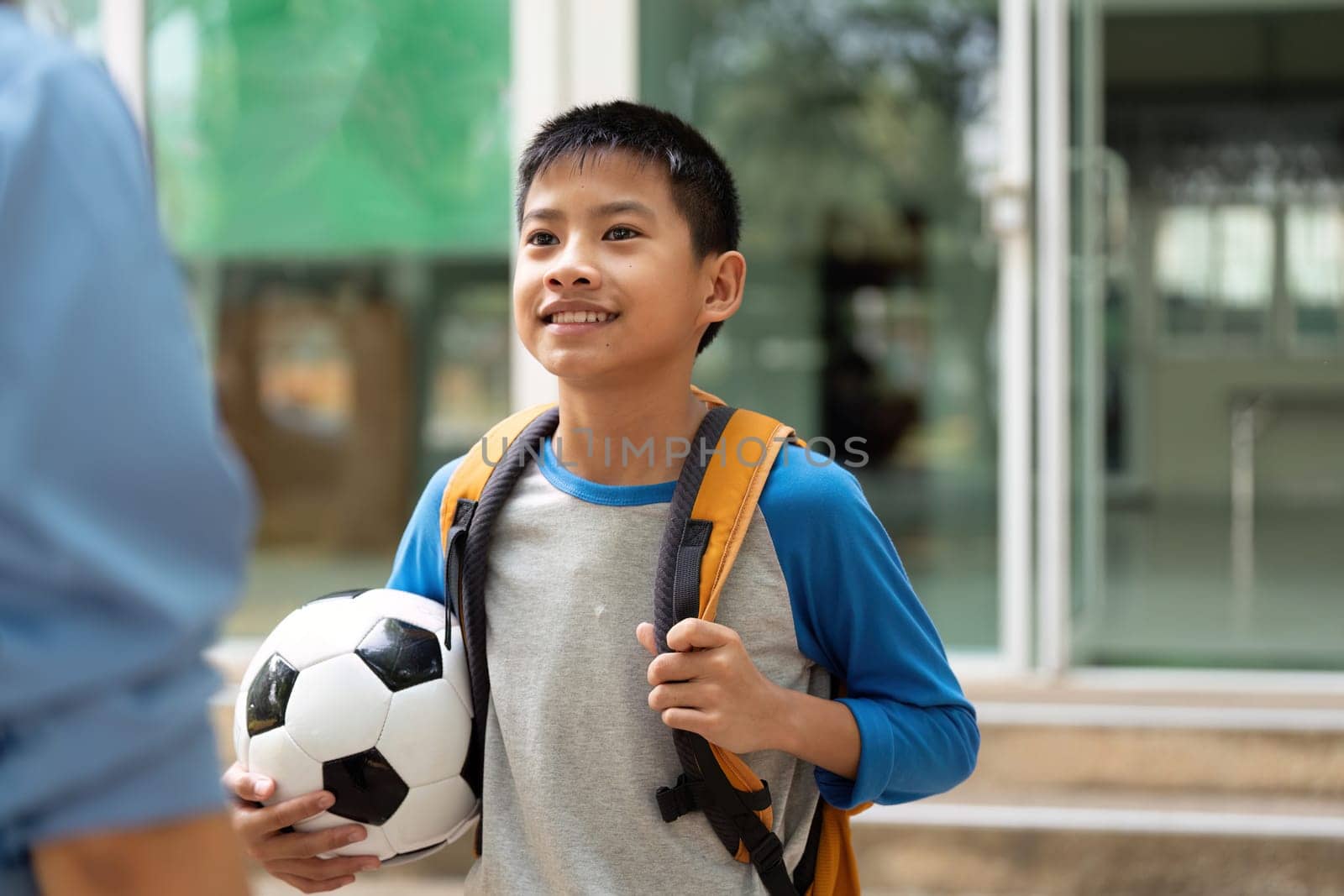 With a bright smile, a young boy proudly holds his soccer ball as he interacts with his mother after school, ready to share stories and laughter.