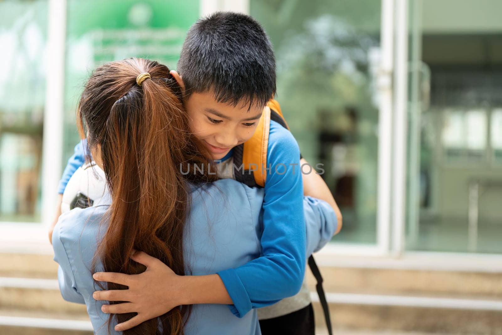 A touching moment unfolds as a young boy with a soccer ball is enveloped in a warm hug from his mother at the school's entrance, celebrating their bond.