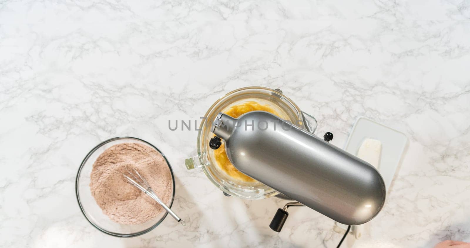Overhead setup with an electric mixer and bowls of prepared dry and wet ingredients for Pale Gingerbread Cookies with Subtle Spice Flavor. A whisk rests in the flour mixture, ready to combine ingredients in the mixer.