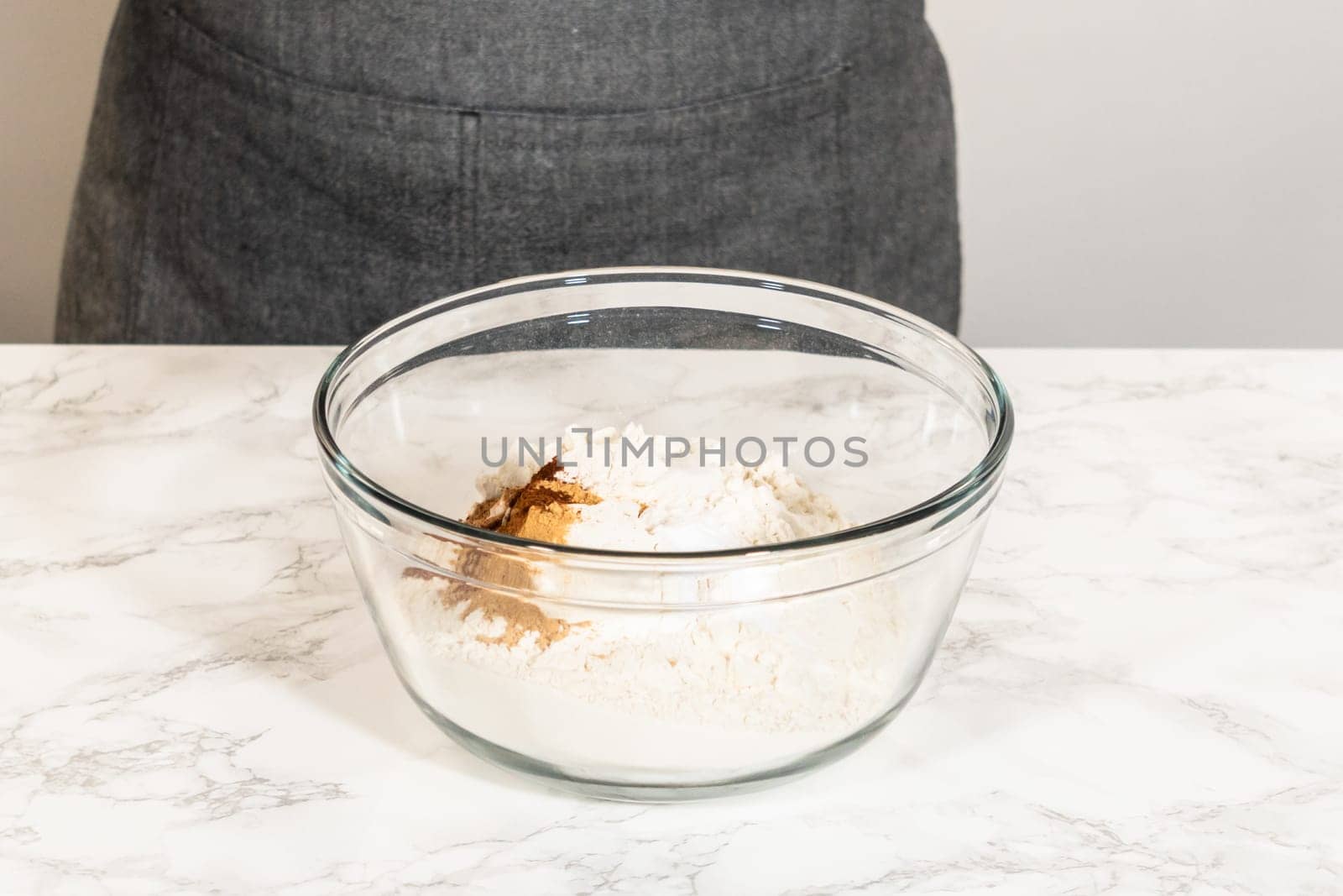 Eye-level view of a mixing bowl containing dry ingredients for Classic Gingerbread Cookie Dough, including flour, baking powder, and spices like cinnamon, ginger, and cloves. These ingredients are ready to be combined, forming the base for the gingerbread dough.