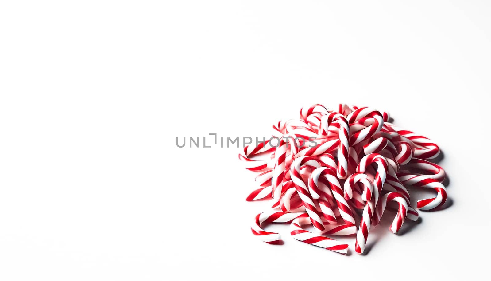 A small pile of neatly rearranged red and white striped candy canes viewed from a slightly elevated angle on a plain white background. This organized heap highlights the candy canes' colorful and festive appearance while maintaining a playful and casual feel.