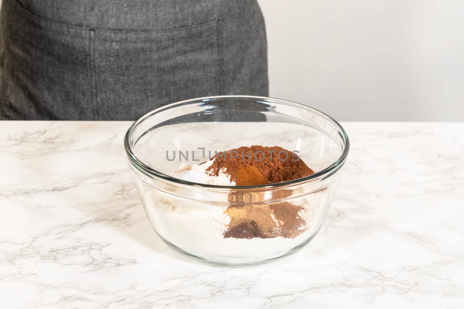 A bowl containing dry ingredients for Chocolate Gingerbread Cookie Dough, including cocoa powder, spices, and flour, ready to be mixed on a marble countertop.
