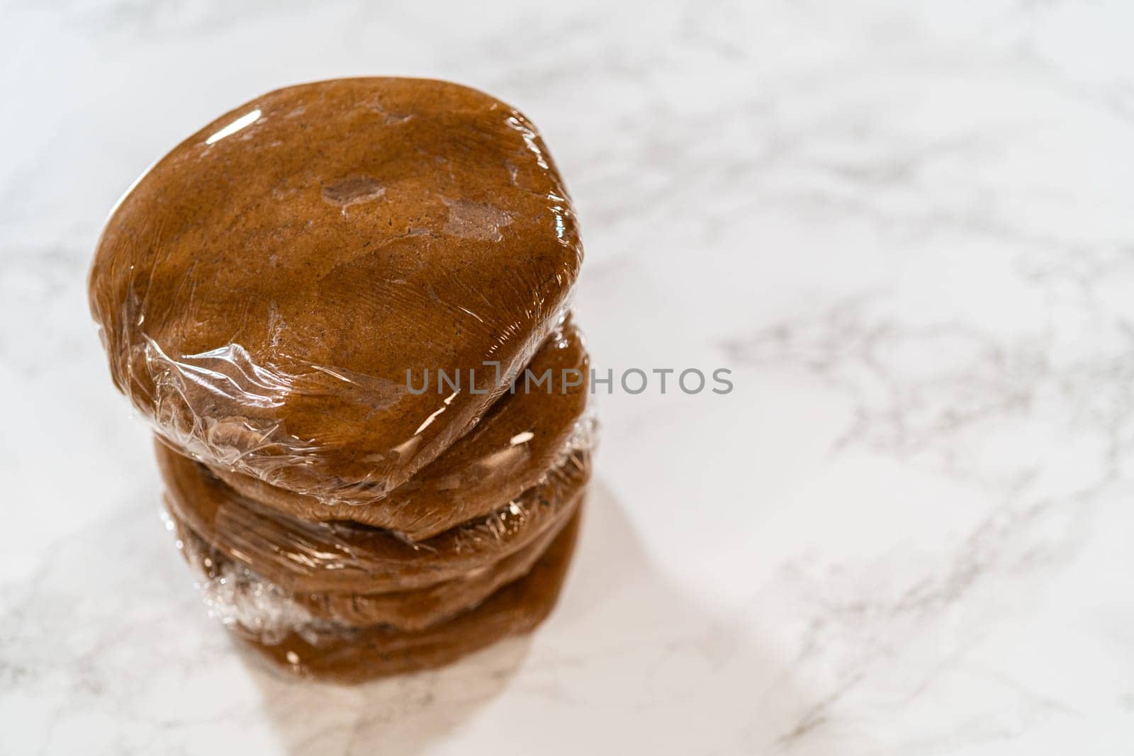 Stacked portions of Spiced Gingerbread Cookie Dough Perfect for Baking wrapped in plastic wrap. The dough is divided for easy handling and chilled, ready for rolling and shaping into cookies.