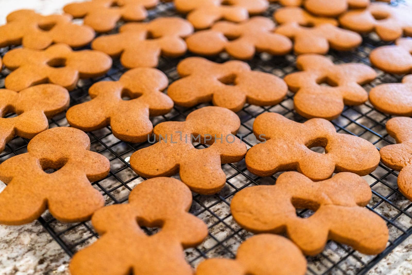 Freshly baked gingerbread cookies find their place on a cooling wire rack in a modern white kitchen, filling the air with festive aromas.