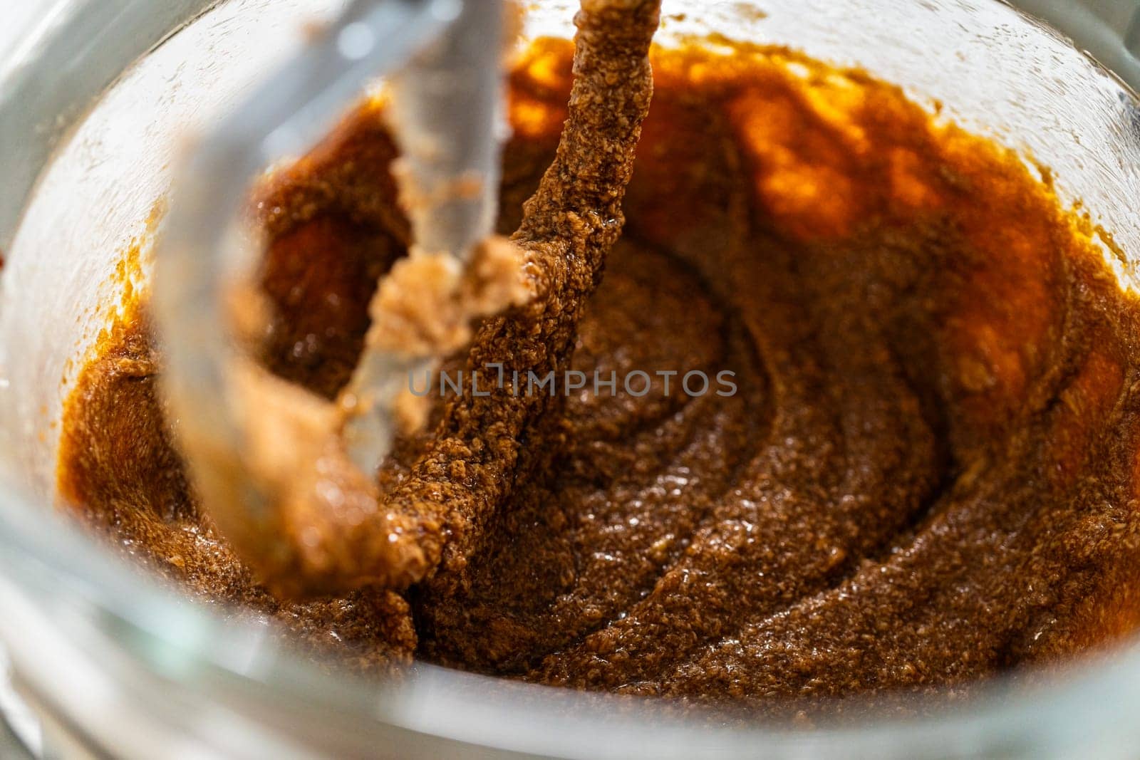 The mixer bowl shows a rich, dark molasses added to the creamed butter and sugar. The molasses is beginning to integrate, creating a deep brown, aromatic mixture.