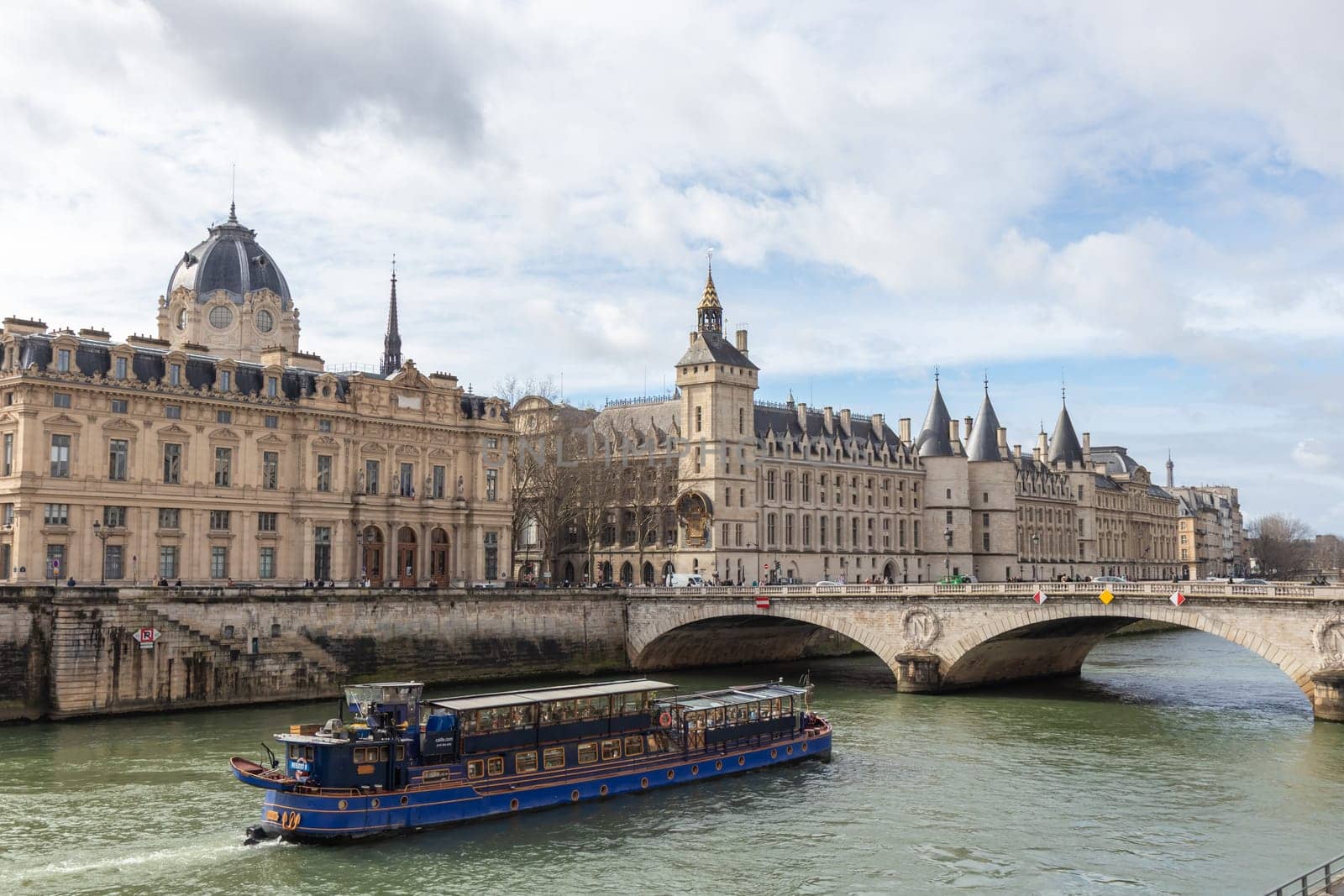 Paris, France - February, 23rd 2025: View of Conciergerie Castle and Bridge of Change over river Seine with beautiful touristic boat. Castle is a former prison, located on west of the Cite Island