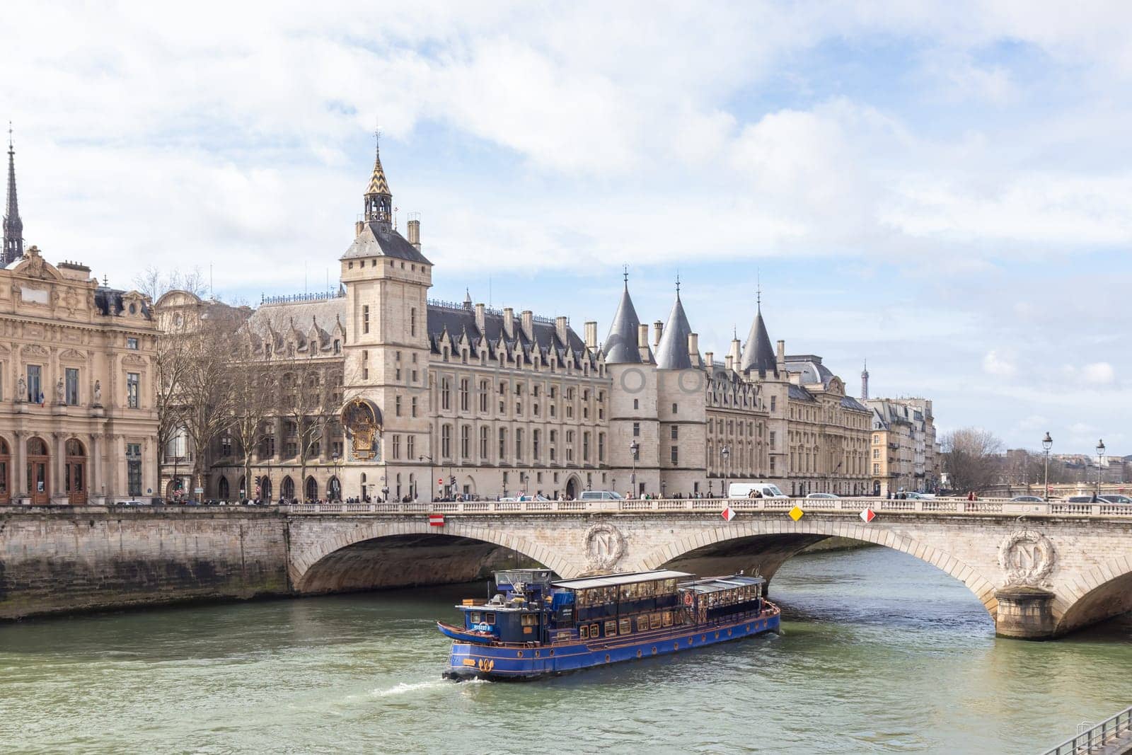 Paris, France - February, 23rd 2025: View of Conciergerie Castle and Bridge of Change over river Seine with beautiful touristic boat. Castle is a former prison, located on west of the Cite Island