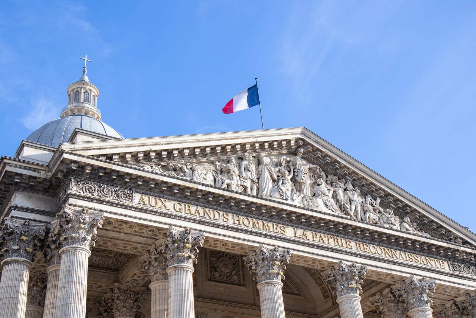 Paris, France - February 22, 2025: A striking view of the Pantheon under a blue sky, showcasing its classical columns and intricate architectural details, topped with the French flag