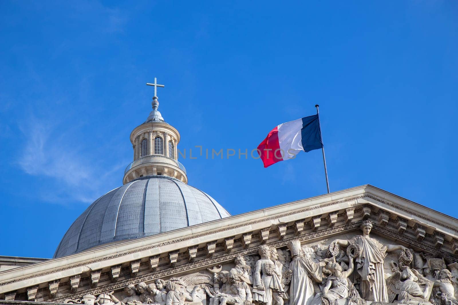 Paris, France - February 22, 2025: A striking view of the Pantheon under a blue sky, showcasing its classical columns and intricate architectural details, topped with the French flag