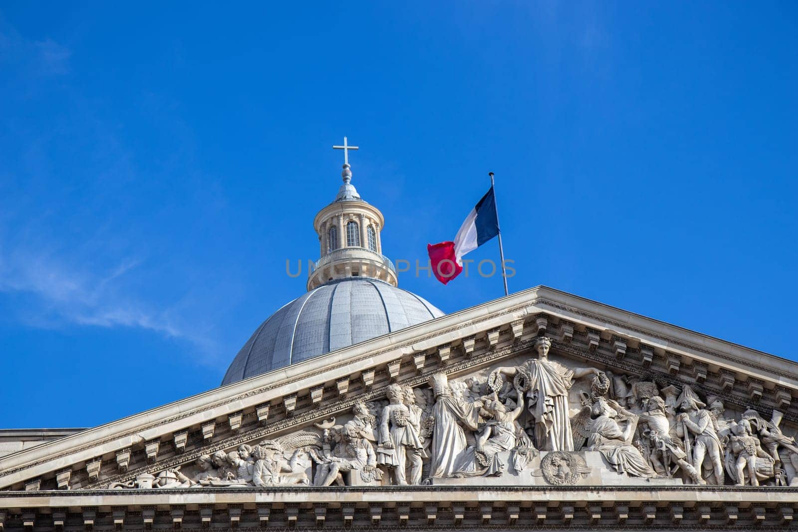 Paris, France - February 22, 2025: A striking view of the Pantheon under a blue sky, showcasing its classical columns and intricate architectural details, topped with the French flag