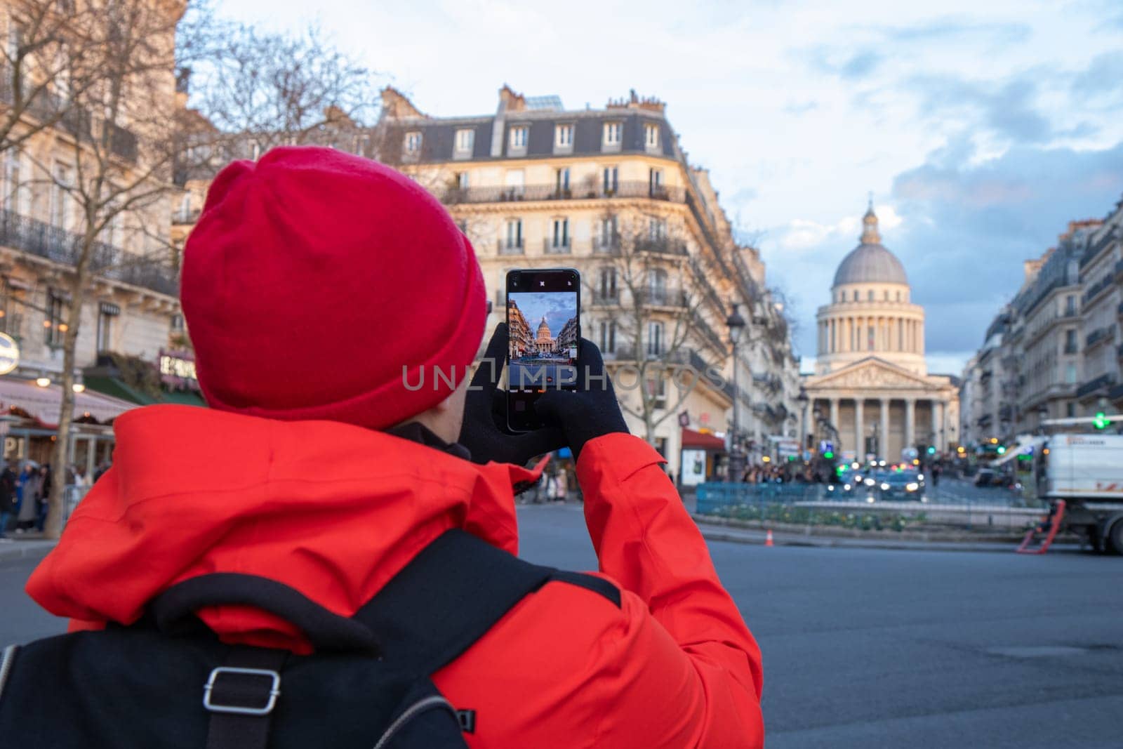 A lonely tourist in red coat takes a photo by his smartphone of the Pantheon in Paris, France, capturing its grand neoclassical architecture and timeless beauty
