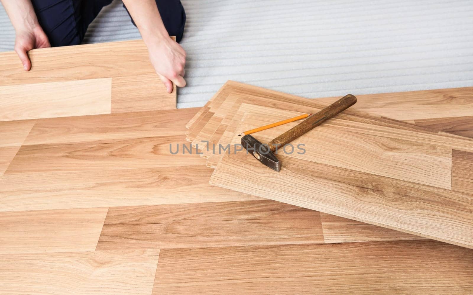 Installing laminated floor, detail on man hands holding wooden tile, over white foam base layer, pencil and hammer near, view from above