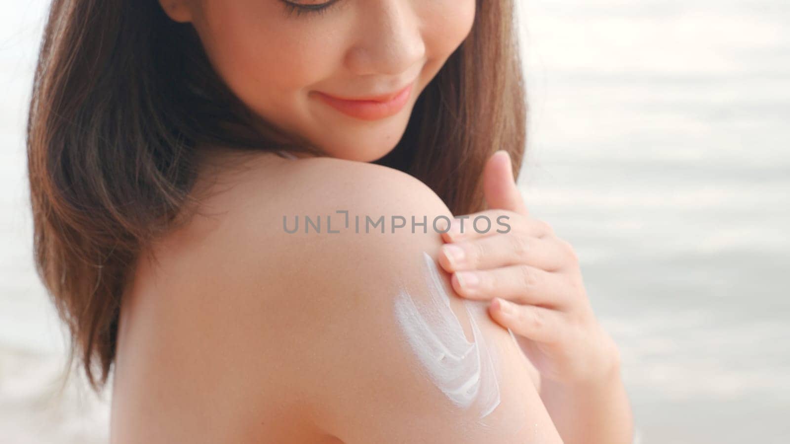 Beautiful Asian woman applying sun protection cream on tanned shoulder on the beach, sun Cream, Close up female in bikini using sunscreen lotion on back body before sunbathing