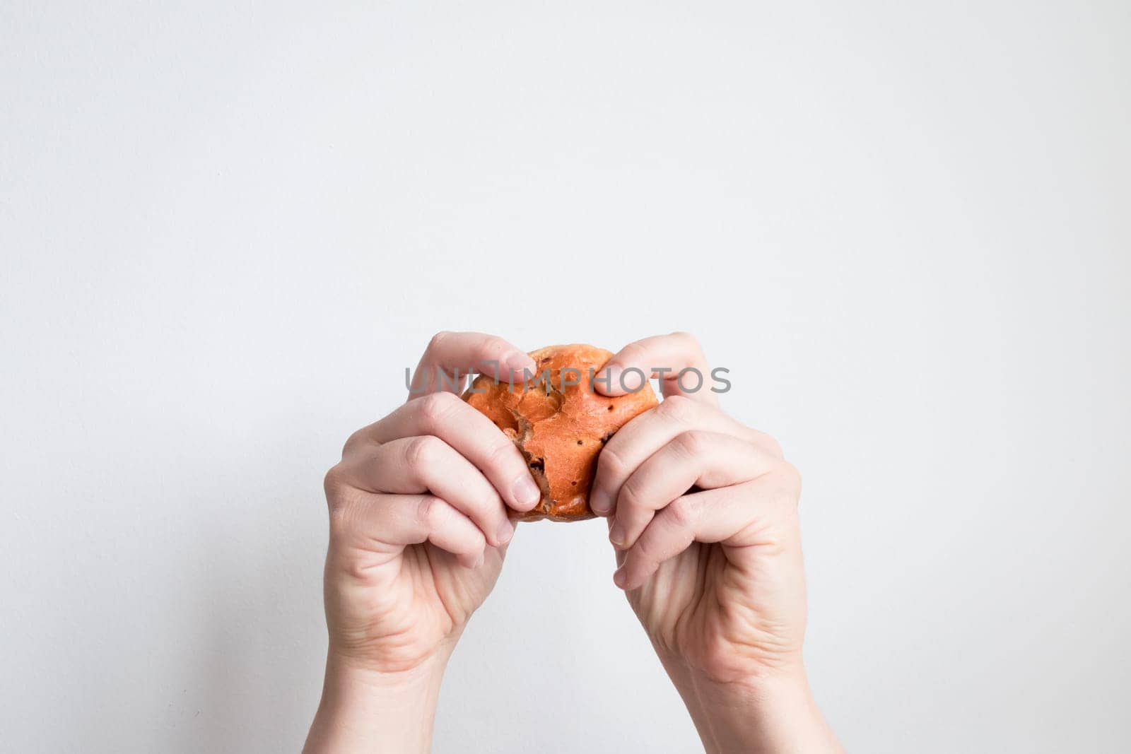 Person holding a freshly baked brown roll with both hands against a white background.