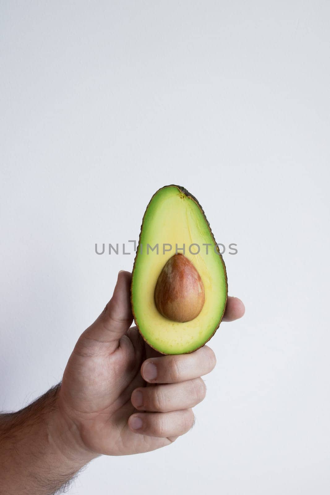 Hand holding fresh ripe avocado against white background.