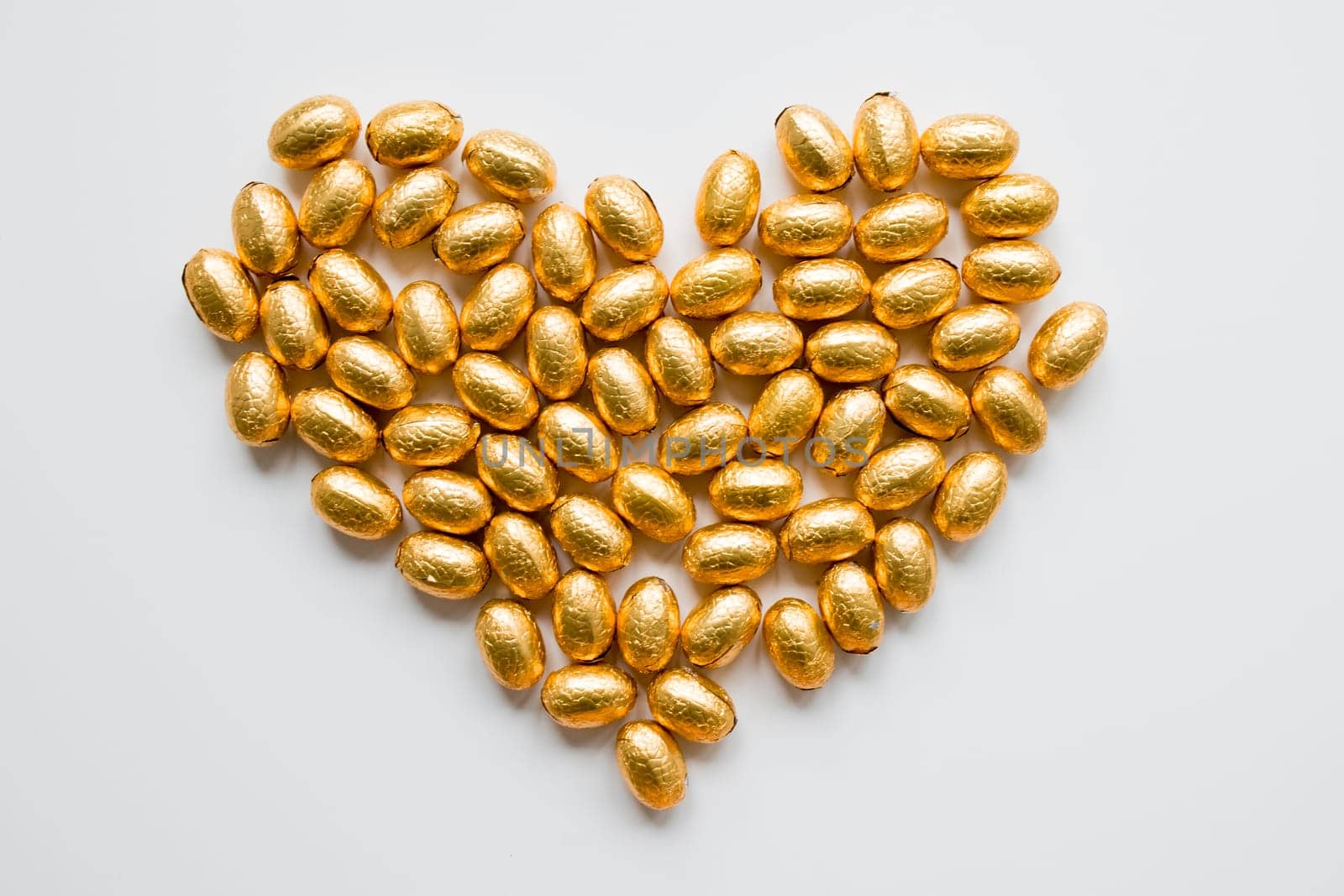 Gold foil wrapped chocolate eggs arranged in heart shape on white background.