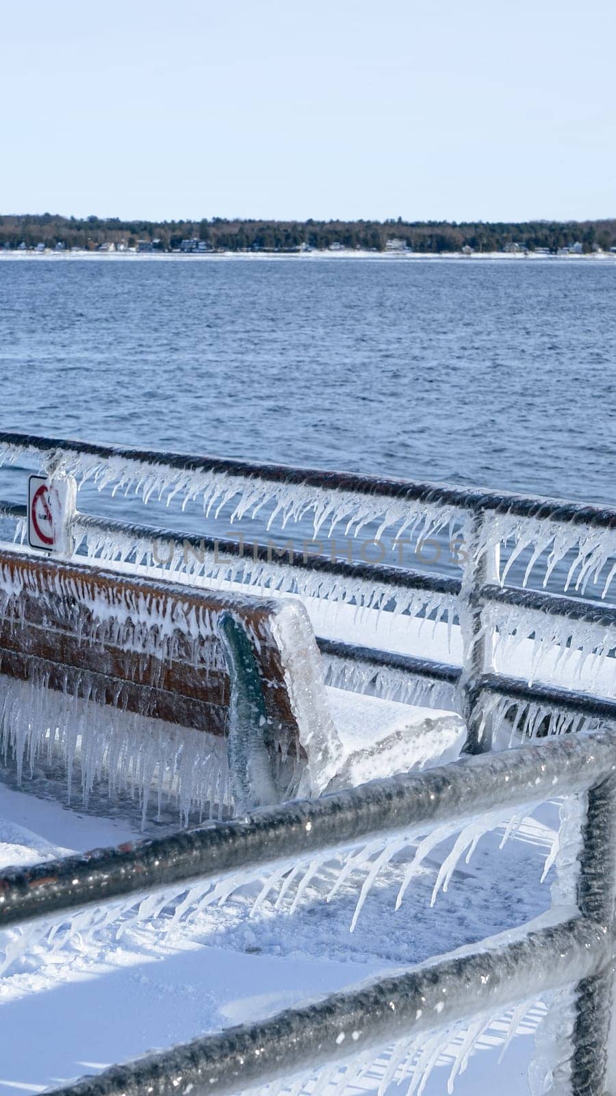 A beautiful wooden bench, adorned with glistening icicles, sits elegantly by the sea. Surrounded by soft, white snow and sparkling ice, it creates a peaceful winter scene, inviting quiet reflection.