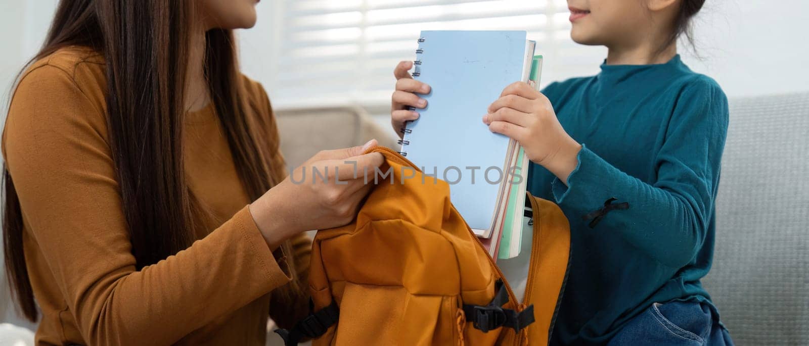 A woman helps a girl gather her school books, showcasing the importance of preparation and learning as they prepare for the school year ahead.