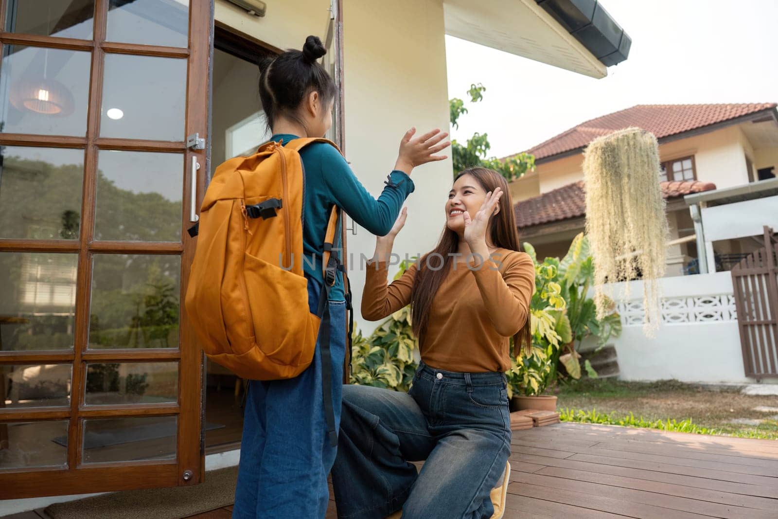 A mother joyfully waves goodbye to her daughter as she heads off to school, capturing the essence of love and encouragement.