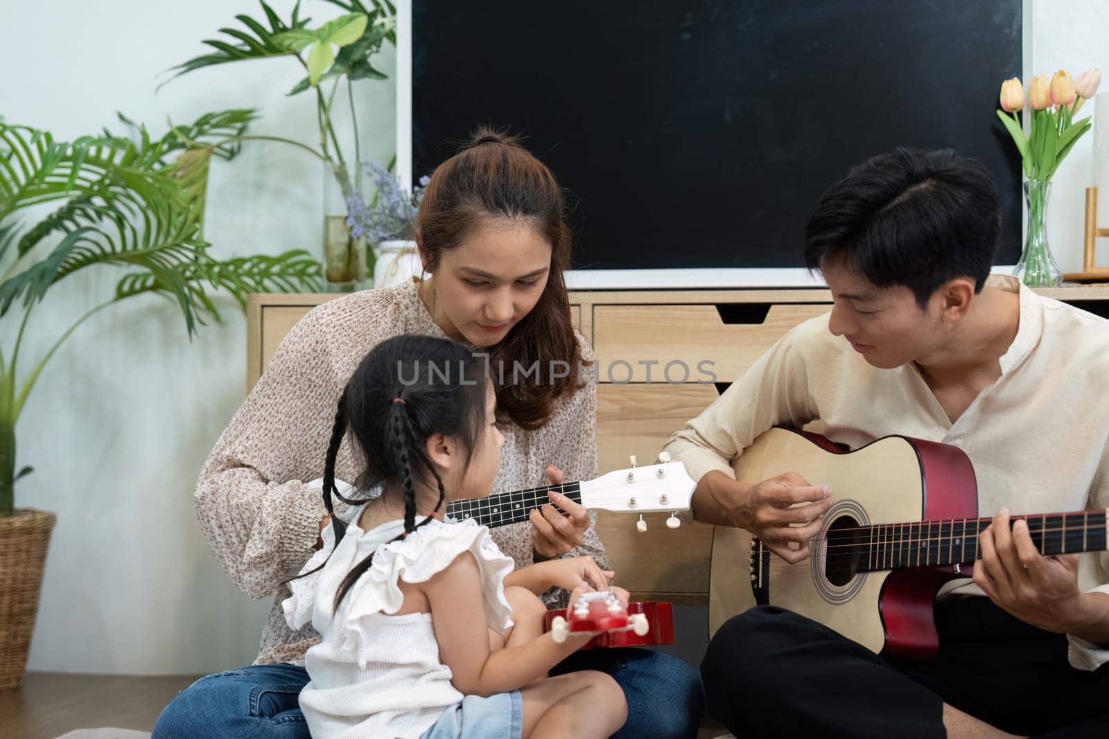 A family moment filled with love as a mother and daughter play musical instruments while a father figures encouragingly by their side.