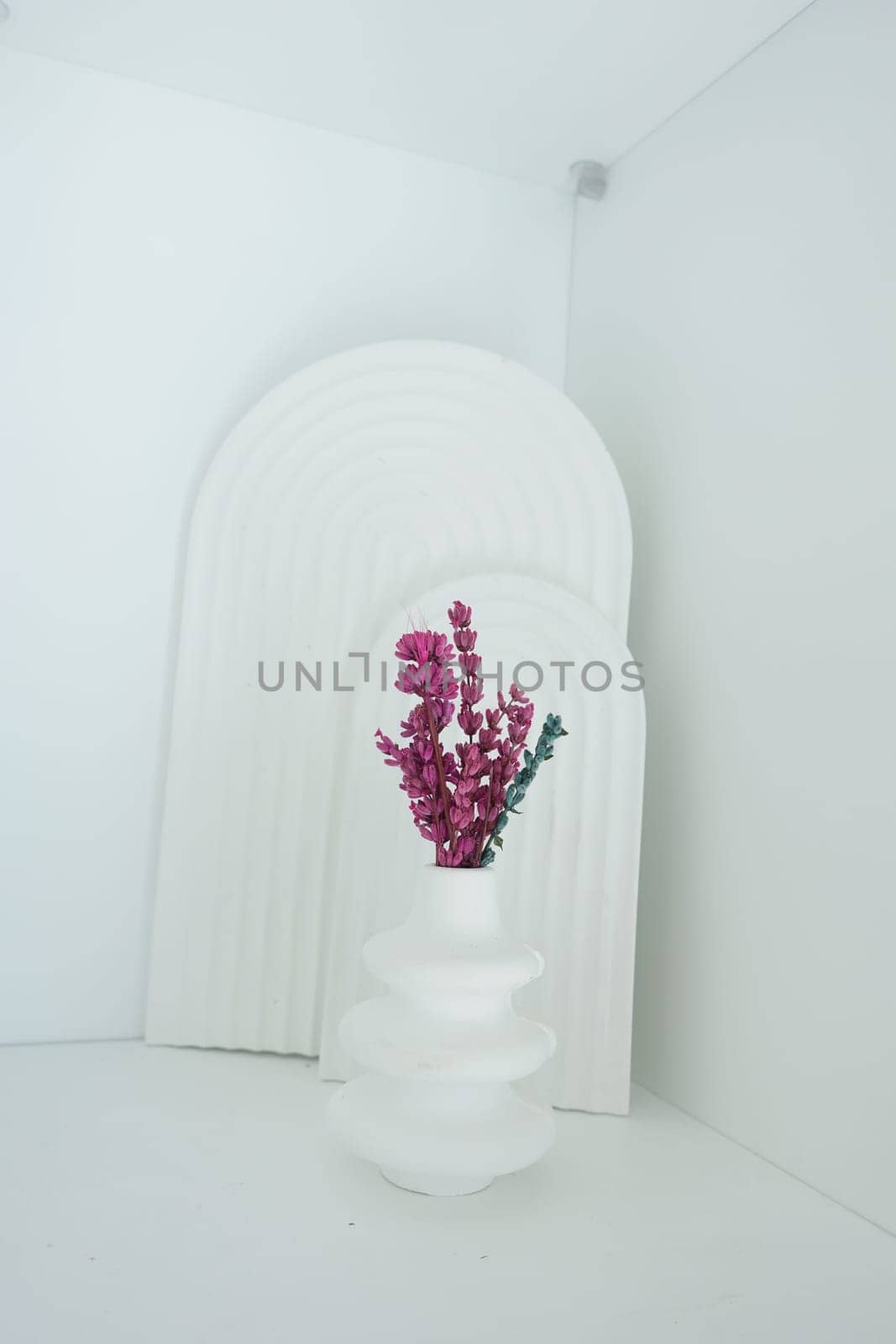 A unique vase holds pink flowers against a white background in a stylish space.