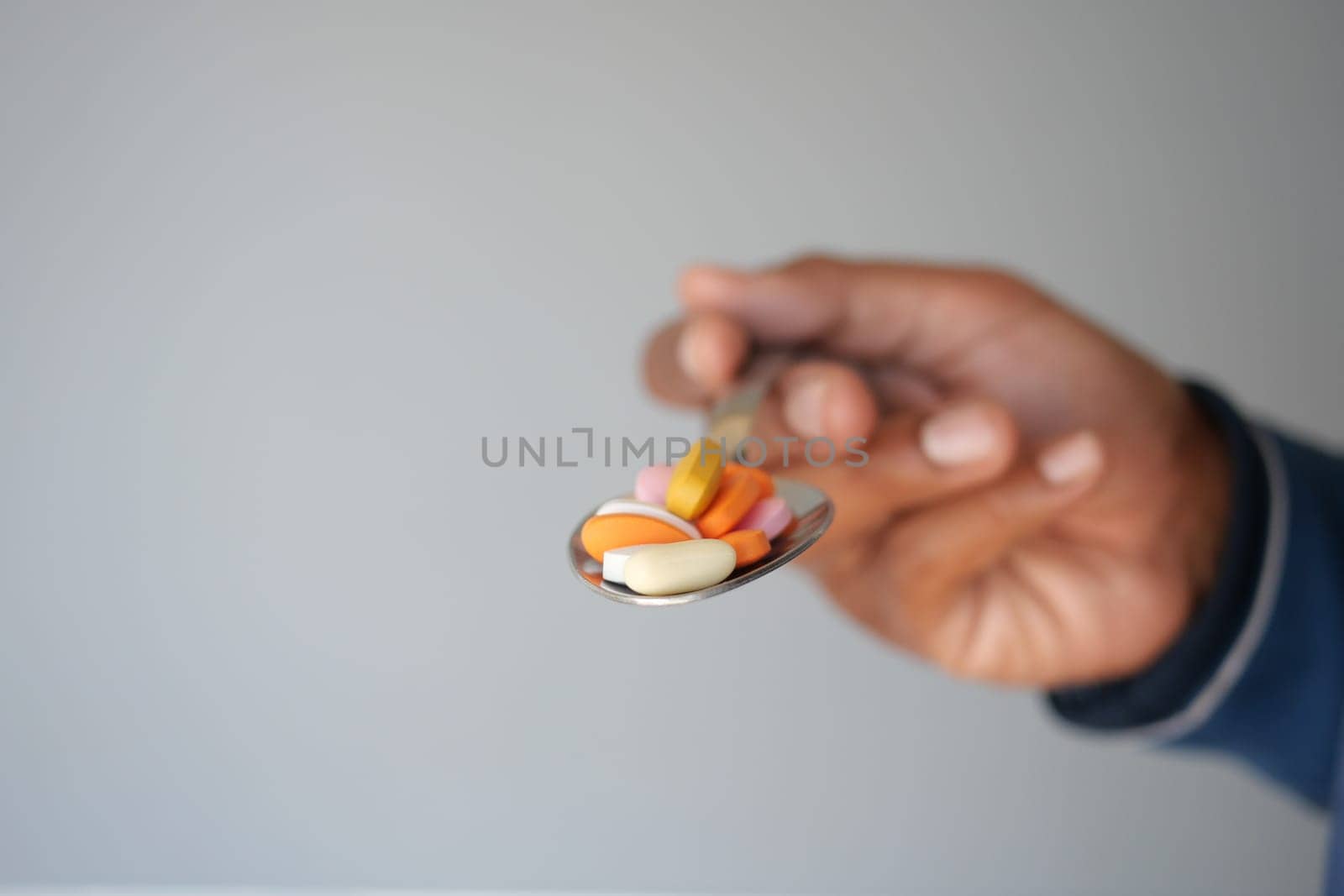 A hand offers a spoon filled with colorful vitamins and supplements.