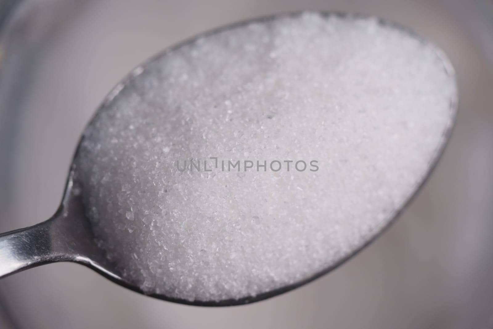 Granulated sugar rests in a metal spoon, highlighting texture and color.